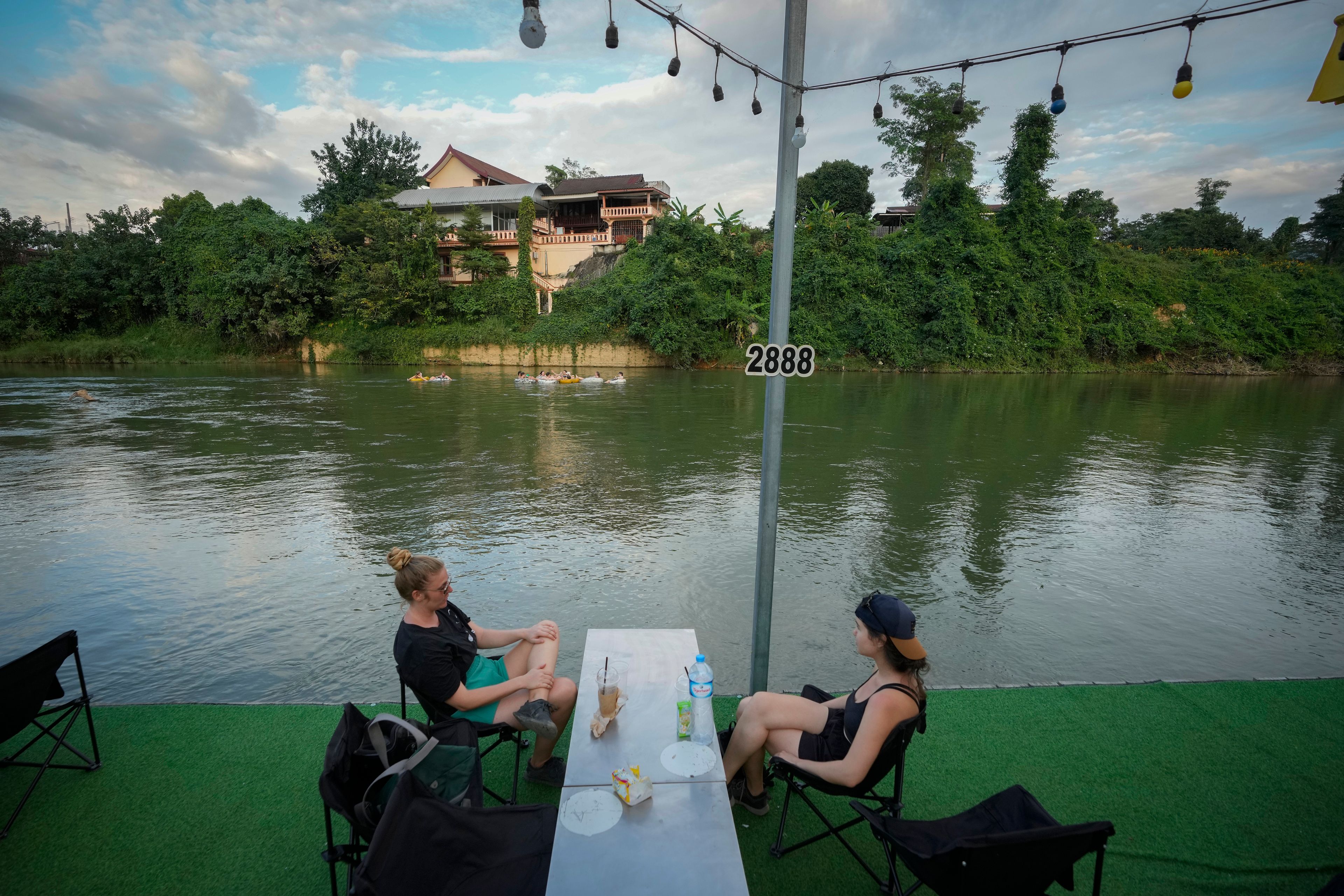 Foreign tourists drink beer at a bar near a river in Vang Vieng, Laos, Tuesday, Nov. 19, 2024. (AP Photo/Anupam Nath)