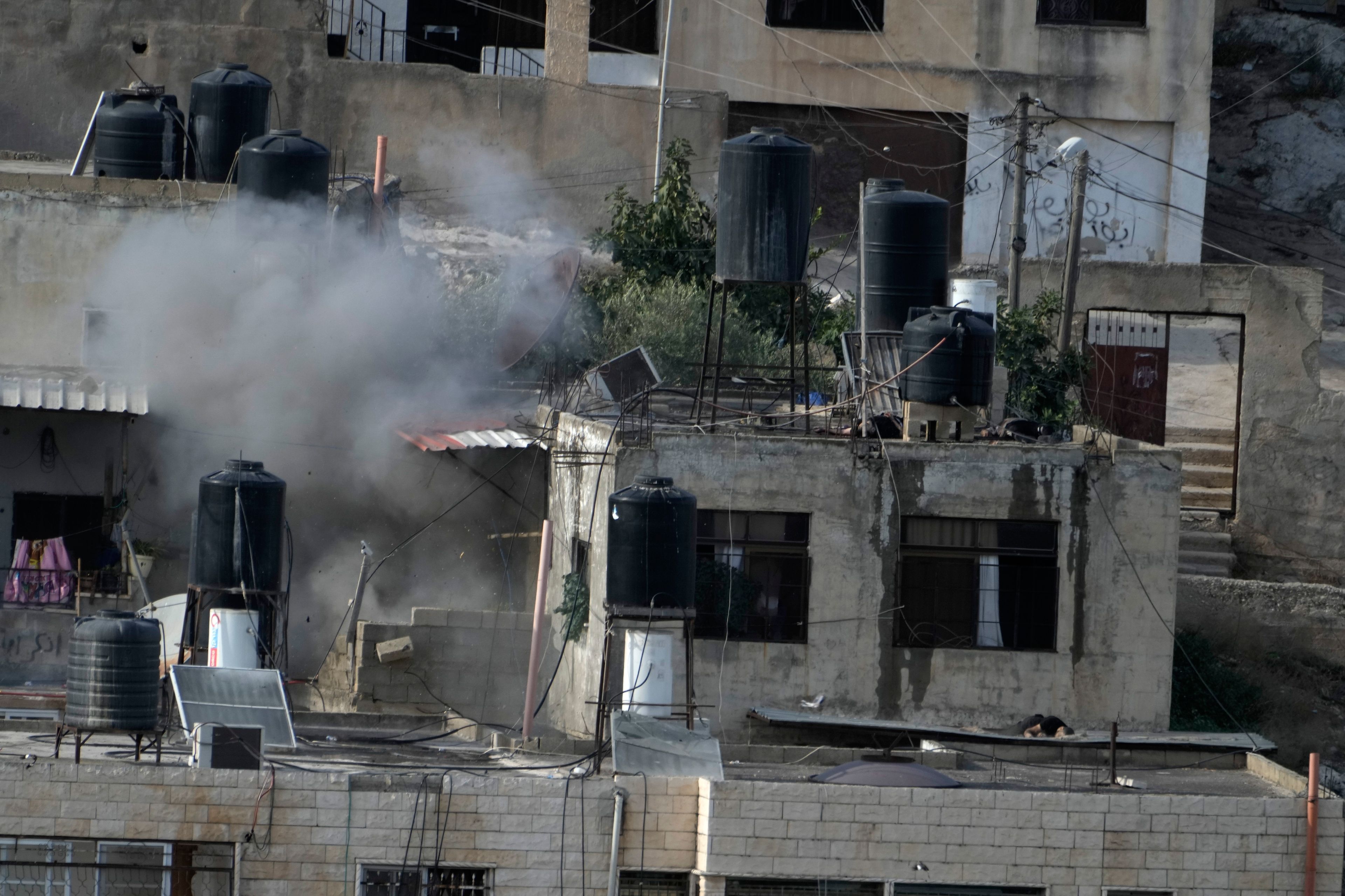 EDS NOTE: GRAPHIC CONTENT - An explosion is seen as three bodies lie motionless on rooftops in the West Bank town of in the West Bank town of Qabatiya during a raid, Thursday, Sept. 19, 2024. (AP Photo/Majdi Mohammed)