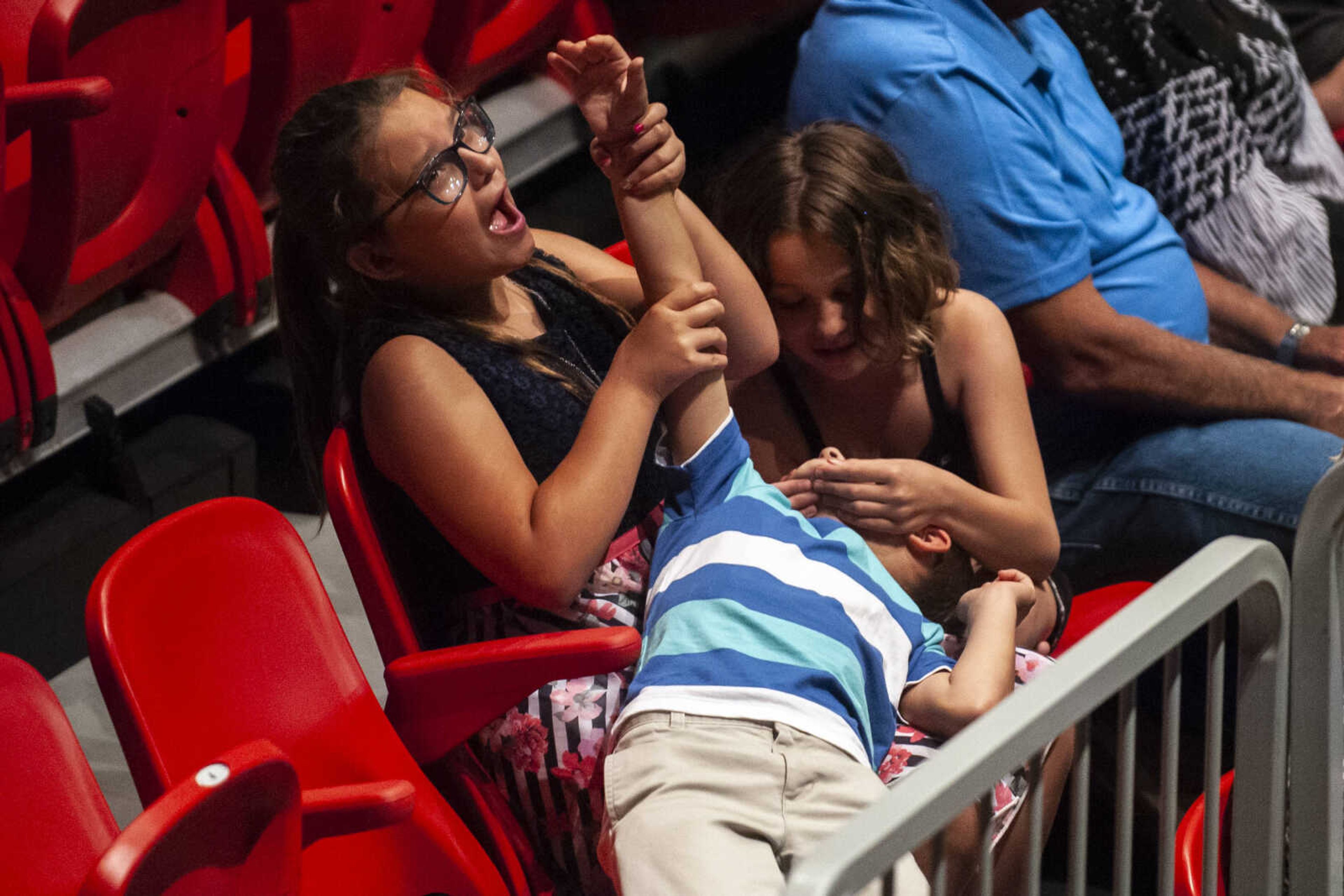 Josie Schwartz, 10, holds her brother Alex Schwartz's, 7, arm up while their cousin Chloe Farmer, 10, plays with Alex's face as they keep themselves busy during the Jackson High School Class of 2019 Commencement at the Show Me Center Friday, May 24, 2019, in Cape Girardeau.