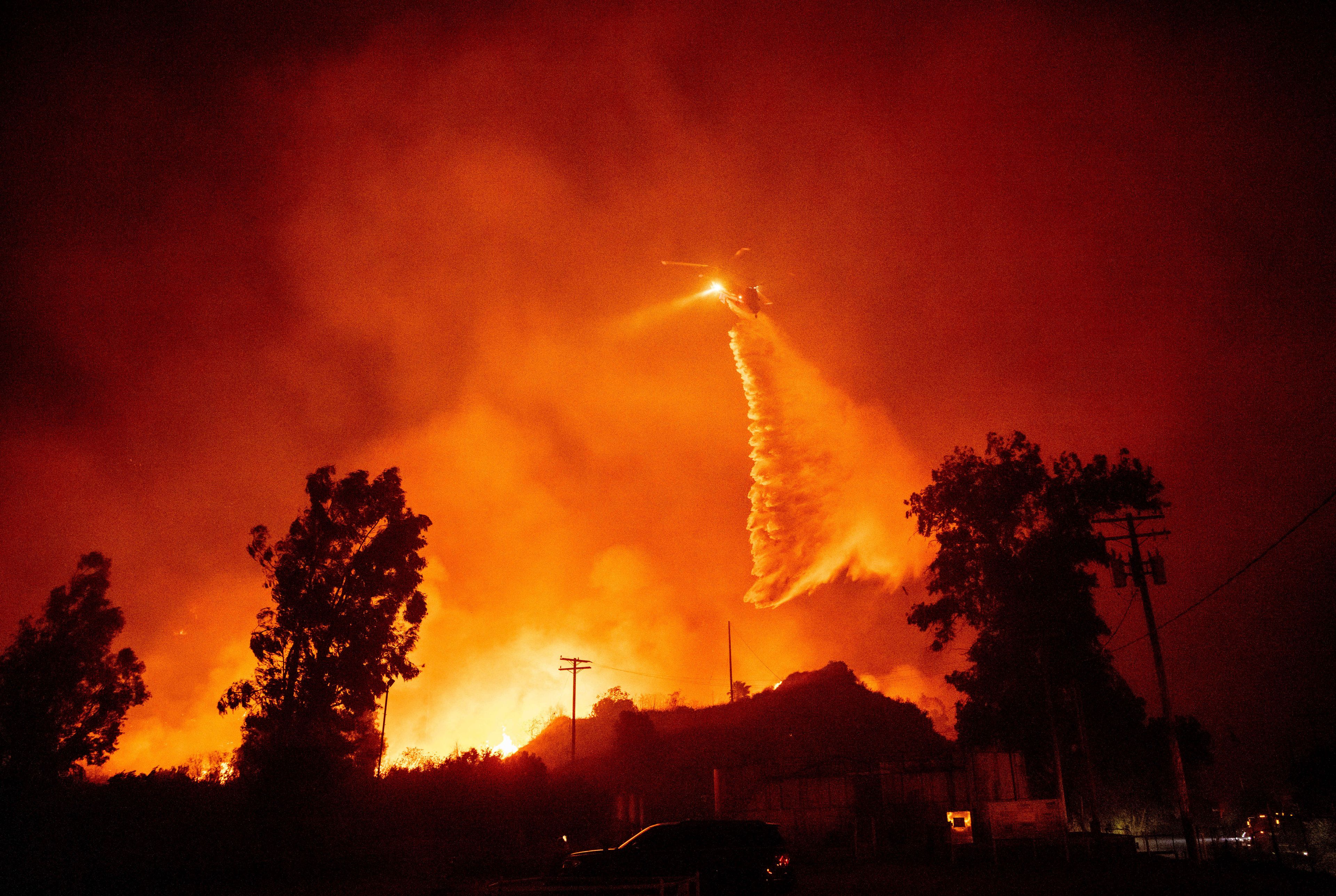 A helicopter drops water over flames in the Mountain fire, Wednesday, Nov. 6, 2024, near Santa Paula, Calif. (AP Photo/Ethan Swope)