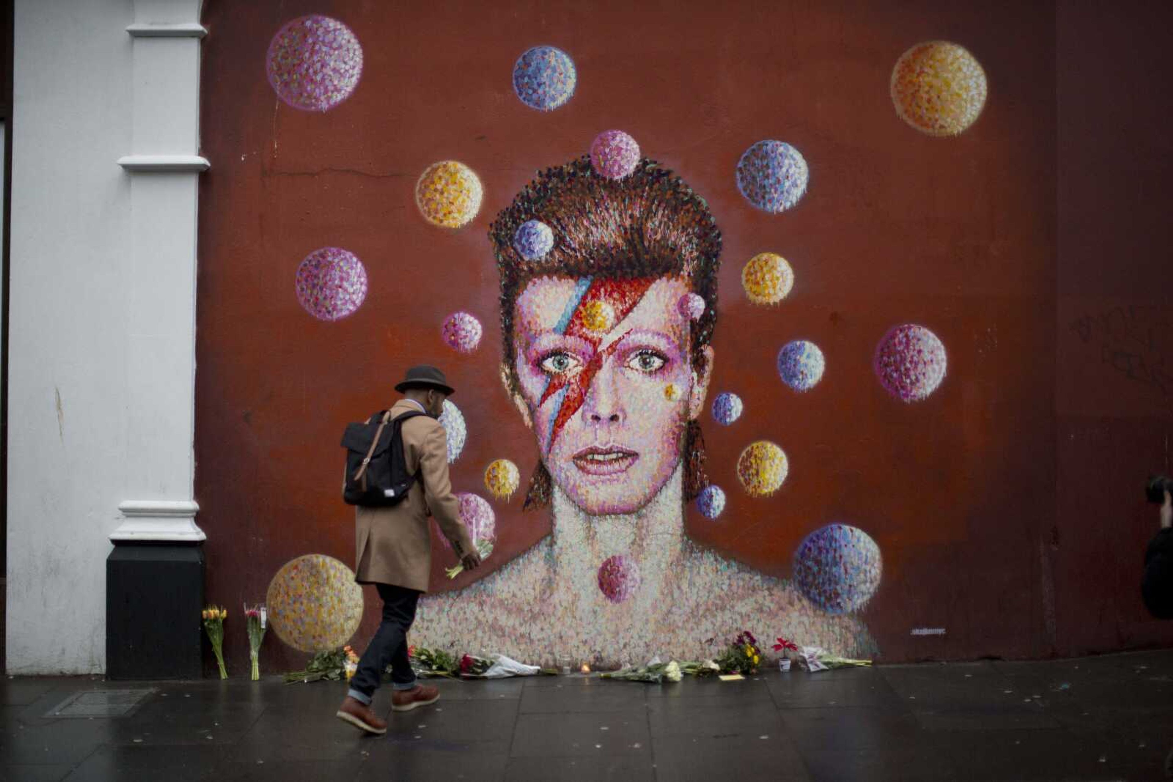 A man walks to place flowers alongside other tributes Monday beside a mural of British singer David Bowie by artist Jimmy C in London. (Matt Dunham ~ Associated Press)