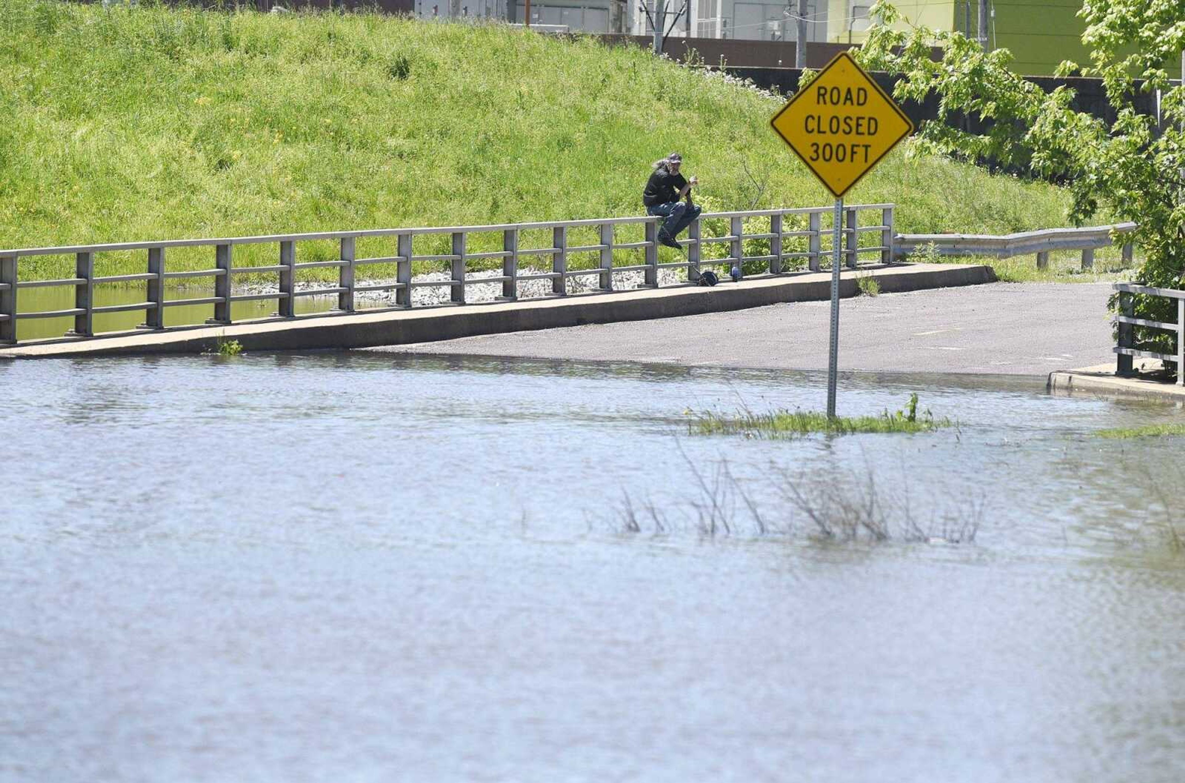 A man sits on a rail of a flooded bridge Tuesday in the Red Star District of Cape Girardeau.