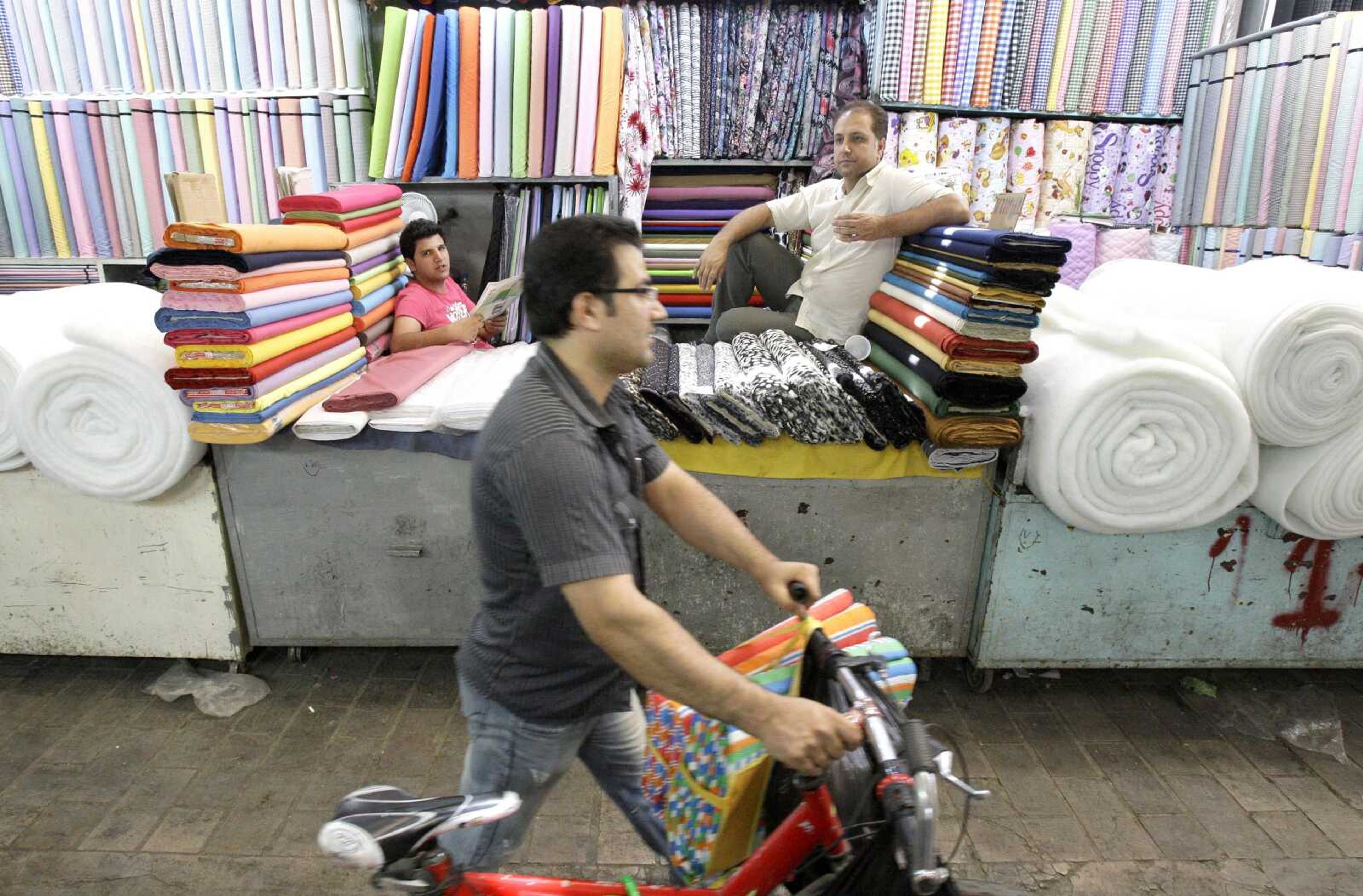 An Iranian man with a bike walks at the main bazaar in Tehran, Iran, as two textile merchants wait for customers July 14. Police threatened merchants who closed their shops in Tehran&#8217;s main bazaar and launched crackdowns on sidewalk money changers Wednesday as part of a push to halt the plunge of Iran&#8217;s currency, which has shed more than a third its value in less than a week. (Vahid Salemi ~ Associated Press)