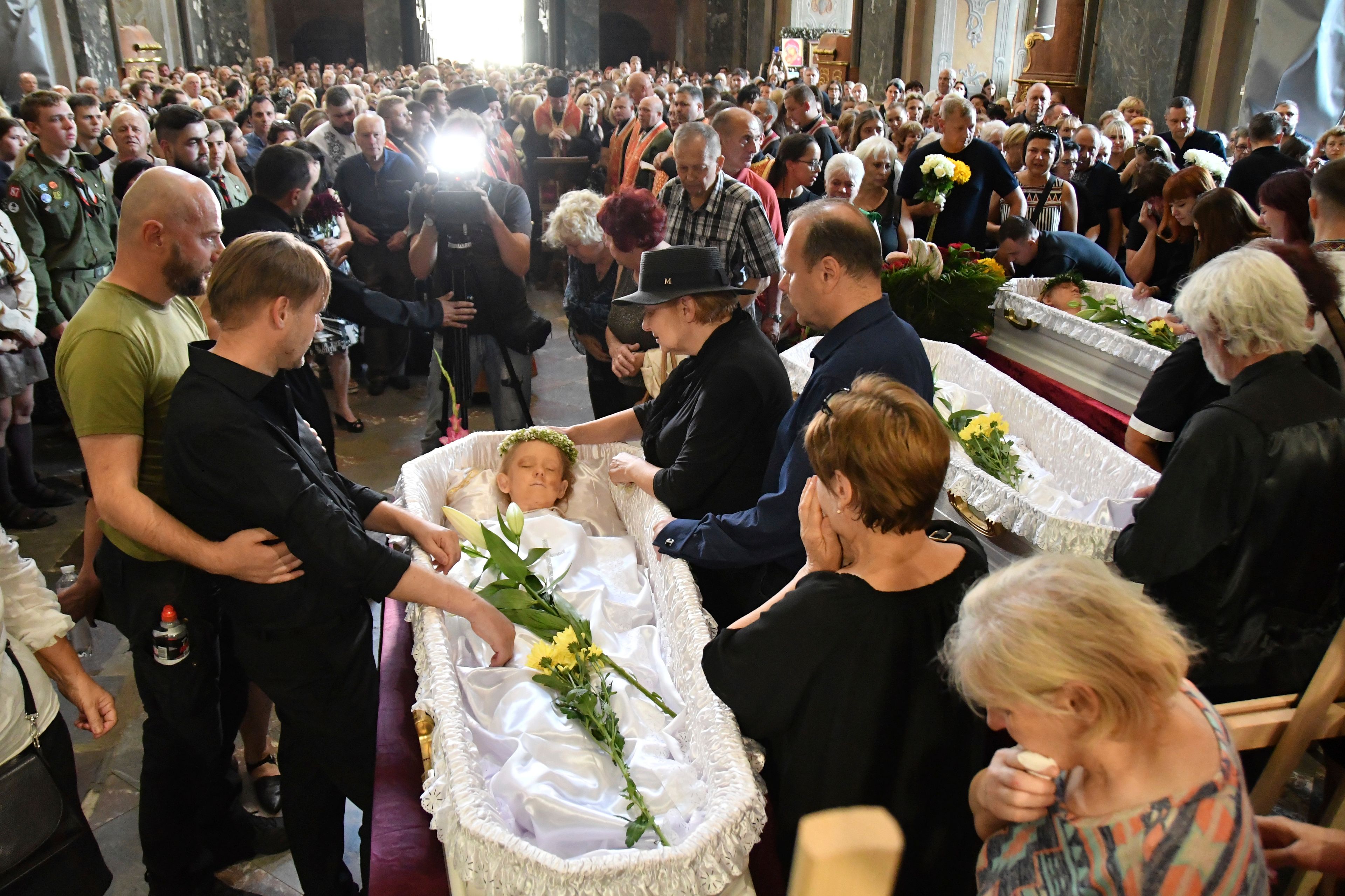 People mourn near the coffins of Yaroslav Bazylevych's, second left, family members during their funeral service in the Garrison Church in Lviv, Ukraine, Friday, Sept. 6, 2024. (AP Photo/Mykola Tys)