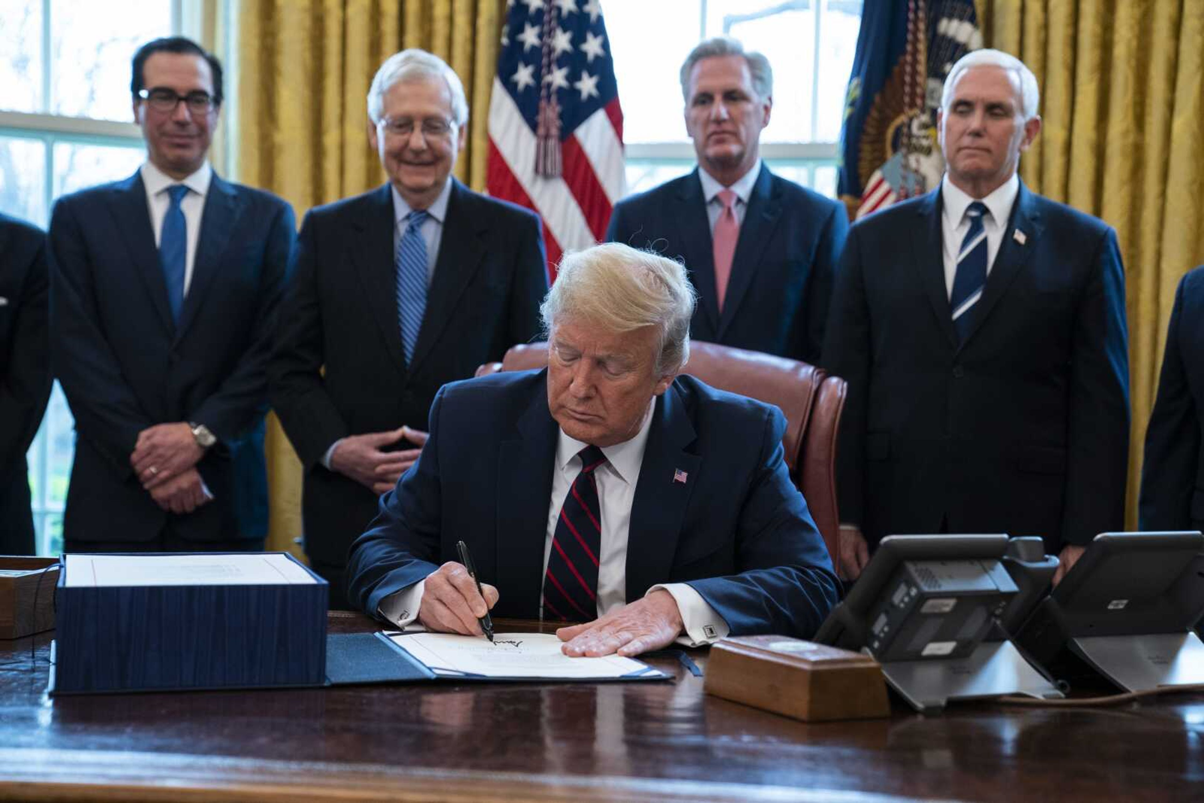 President Donald Trump signs the coronavirus stimulus relief package in the Oval Office at the White House, Friday, March 27, 2020, in Washington, as Treasury Secretary Steven Mnuchin, Senate Majority Leader Mitch McConnell, R-Ky., House Minority Leader Kevin McCarty, R-Calif., and Vice President Mike Pence watch. (AP Photo/Evan Vucci)