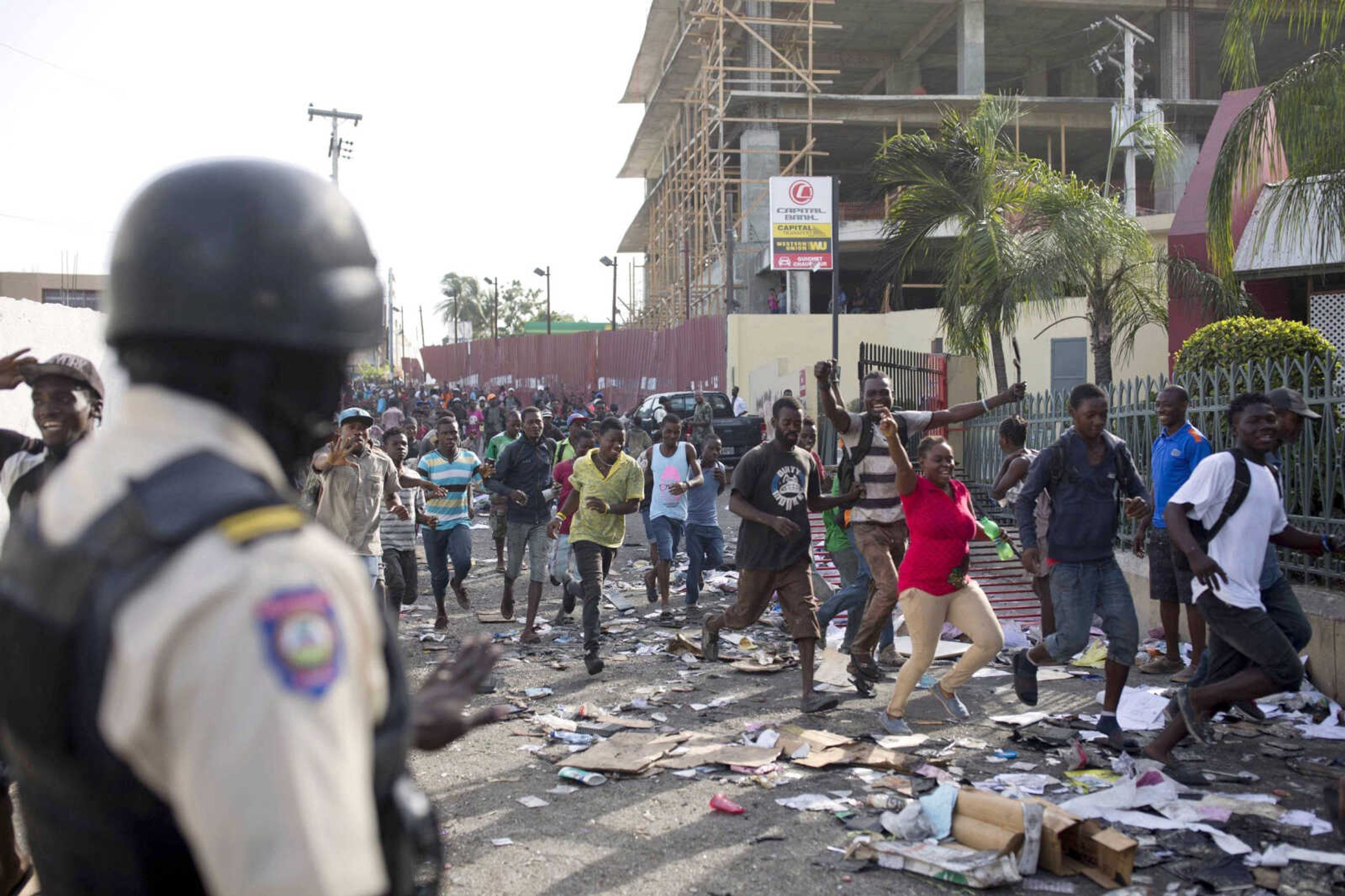 A police officer looks on as a crowd enters the Delimart supermarket complex Sunday in Port-au-Prince, Haiti.