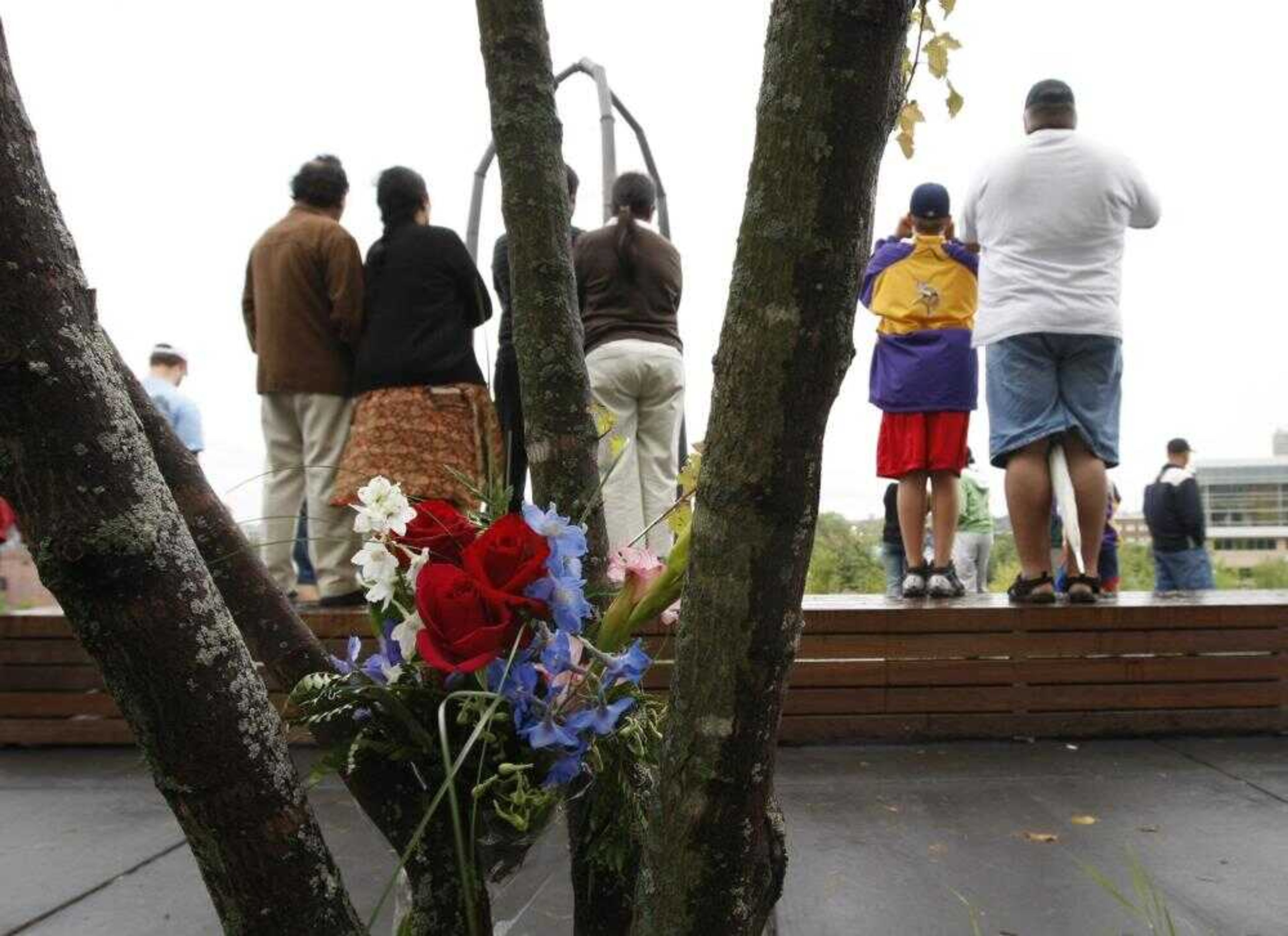 Flowers are placed in trees as a memorial to those lost in the collapse of the Interstate 35W bridge, as people gather on a hill to view the scene at Gold Medal Park in Minneapolis, Saturday, Aug. 4, 2007.  (AP Photo/Gerald Herbert)