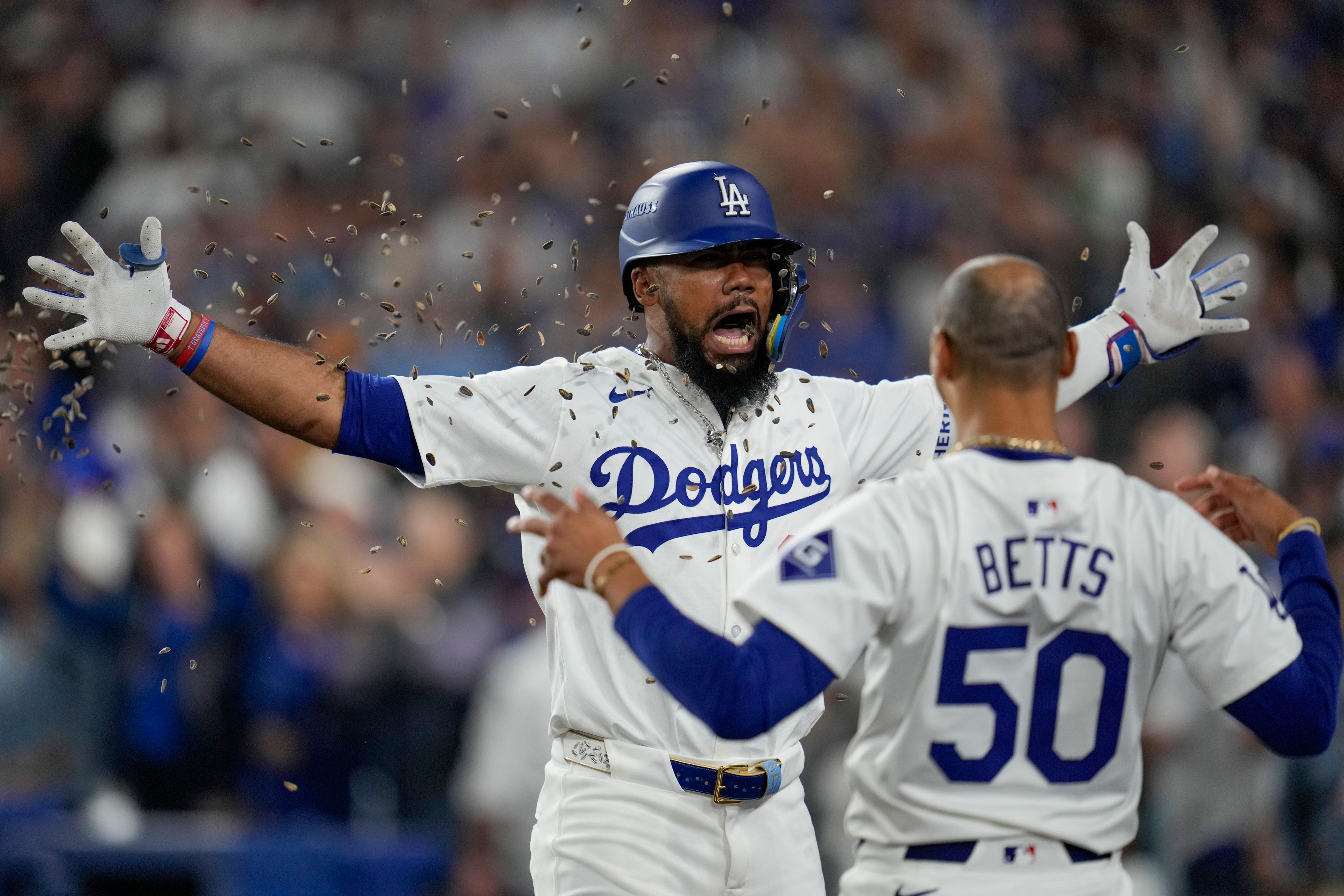 Los Angeles Dodgers' Teoscar Hernández, left, gets sunflower seeds to the face to celebrate his solo home run as Mookie Betts (50) looks on during the seventh inning in Game 5 of a baseball NL Division Series against the San Diego Padres, Friday, Oct. 11, 2024, in Los Angeles. (AP Photo/Ashley Landis)