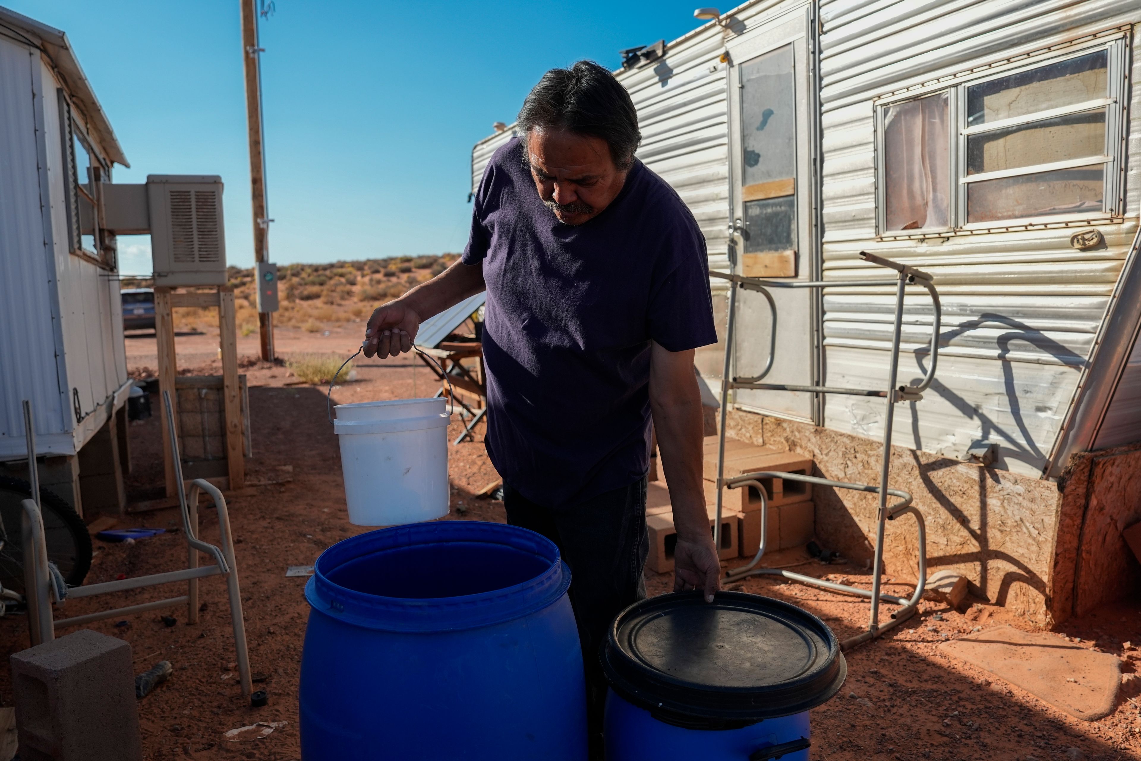 Ricky Gillis collects water for use in a evaporative air cooling unit, at left, Wednesday, Oct. 9, 2024, at his home on the Navajo Nation in Halchita, Utah. (AP Photo/Joshua A. Bickel)