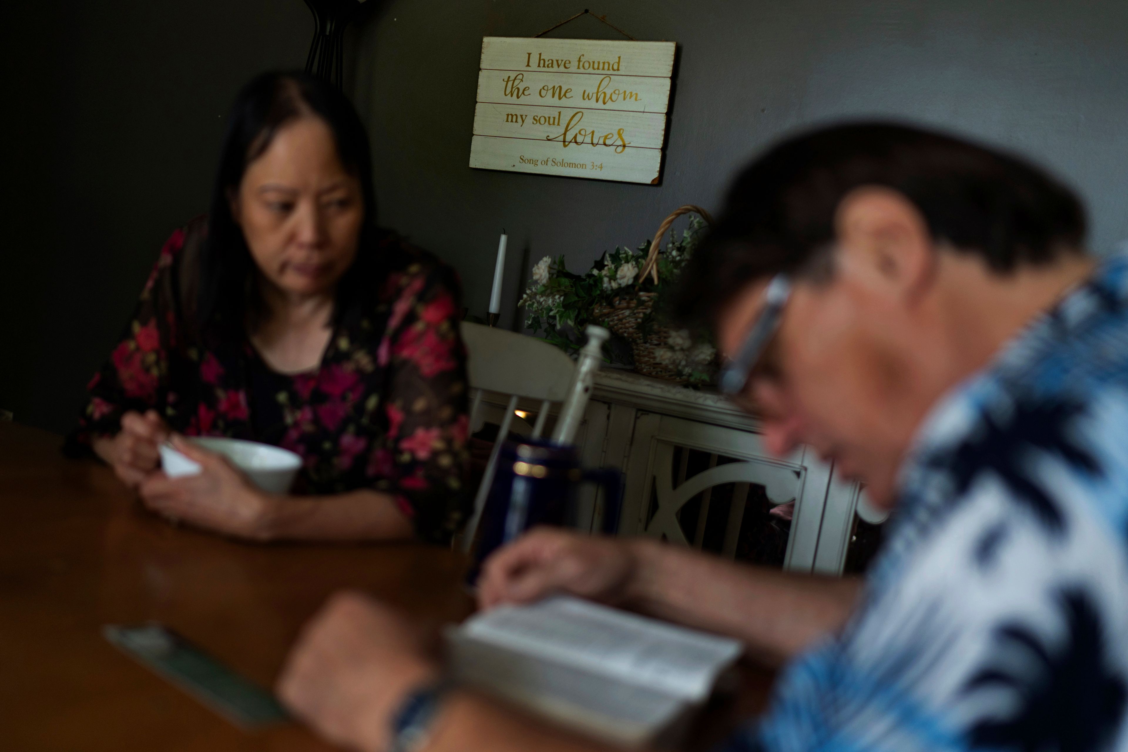 A message decorates the wall behind Lesley, left, and Matt Dzik, as they read the Bible at their home in Champaign, Ill., Sunday, Sept. 22, 2024. When they came across Braver Angels, a nonprofit that helps people bridge the political divide, they found a community there that is both red and blue. "It gave me enough hope," said Lesley. "I felt safe, I'm not alone." (AP Photo/David Goldman)