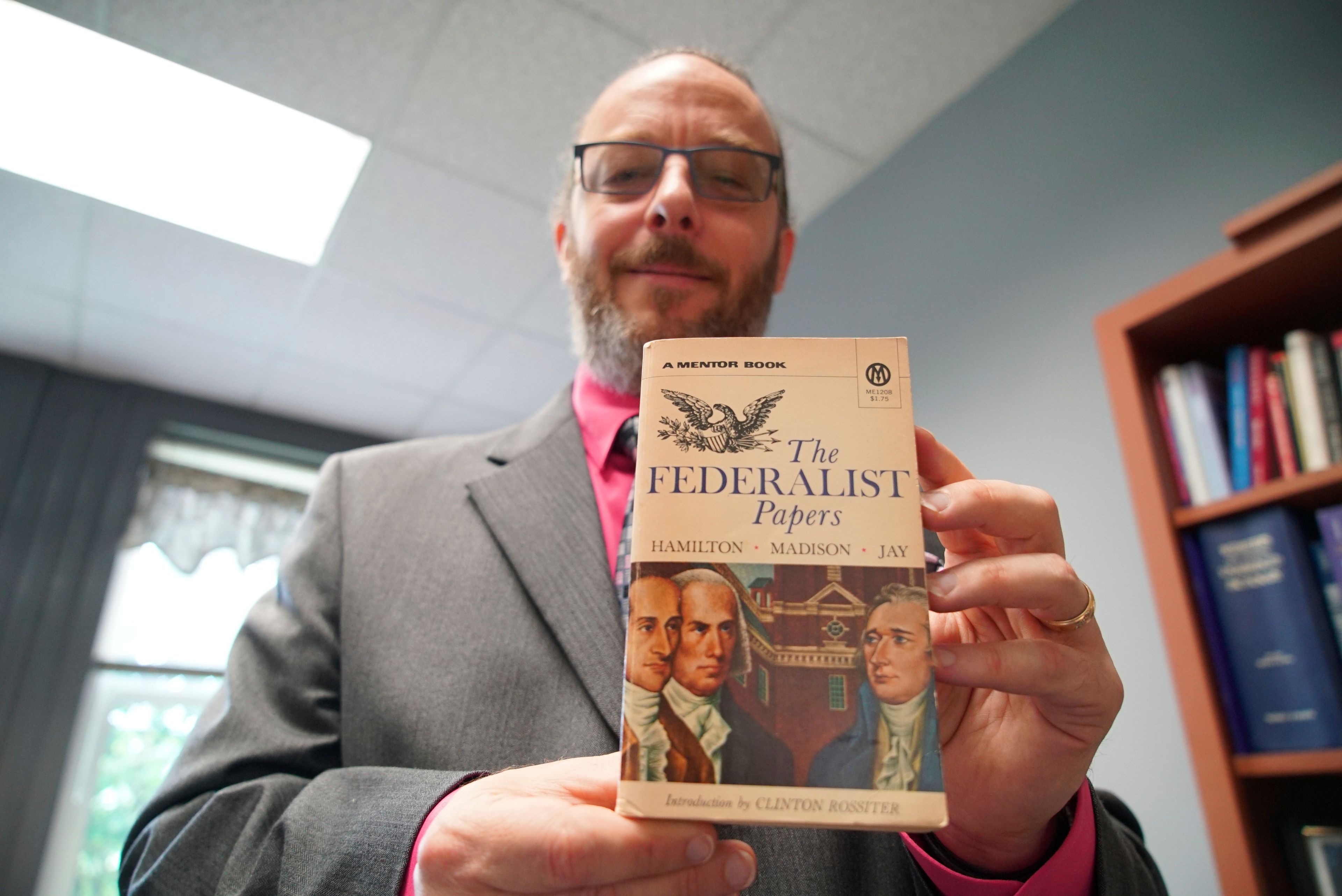 Professor Wade Maki holds up a copy of the book "The Federalist Papers" in his office in Greensboro, N.C., on Wednesday, April 24, 2024. Maki, chairman of the University of North Carolina system's faculty senate, helped draft a civics requirement that students at all publicly funded colleges will have to fulfill starting in July 2025. (AP Photo/Allen G. Breed)