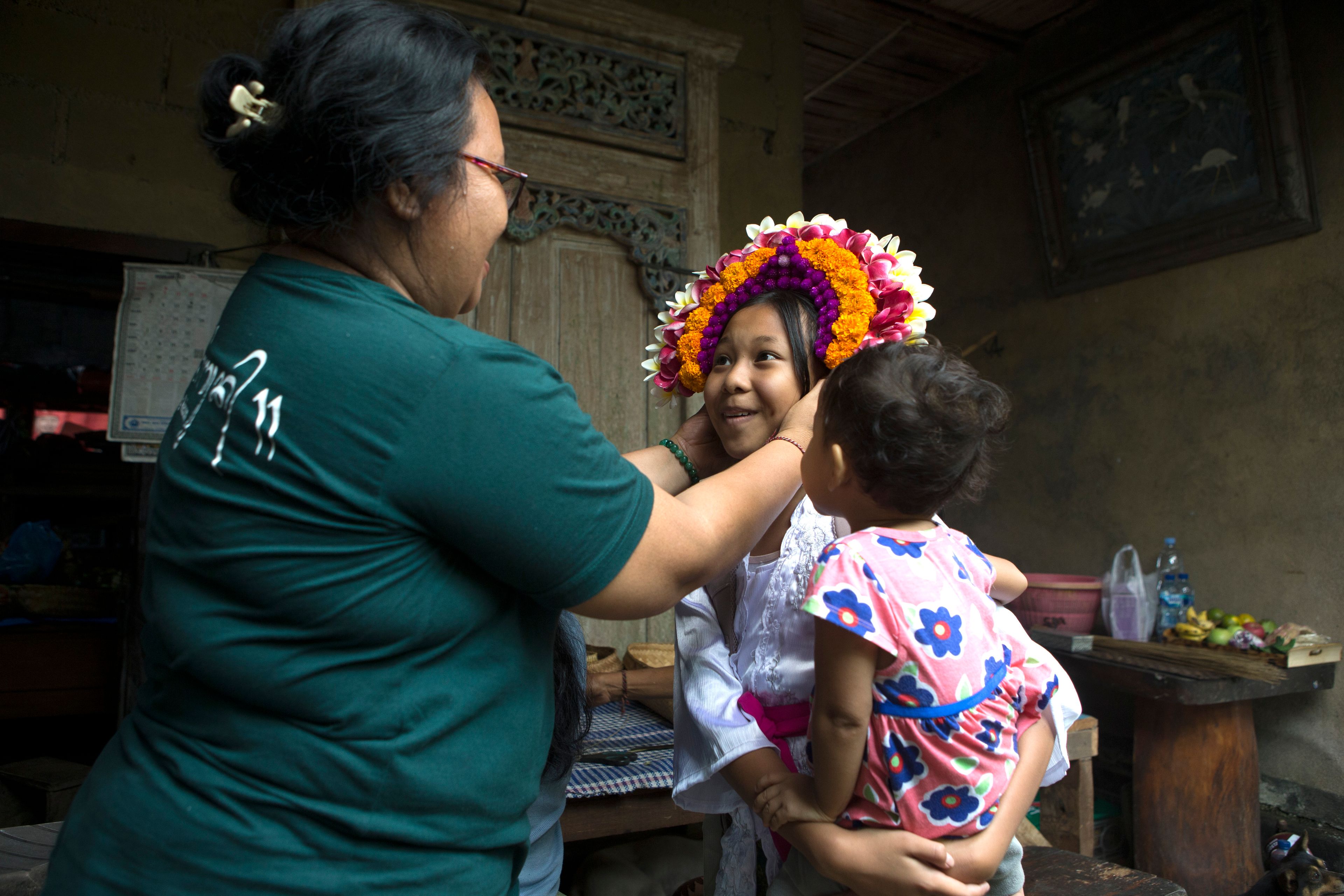 Kadek Krisni, left, tries on a headgear for size on her daughter Kadek Nita Wahyuni in preparation for a Hindu ritual at Geriana Kauh village, Karangasem, Bali, Indonesia on Thursday, Nov. 21, 2024. (AP Photo/Firdia Lisnawati)