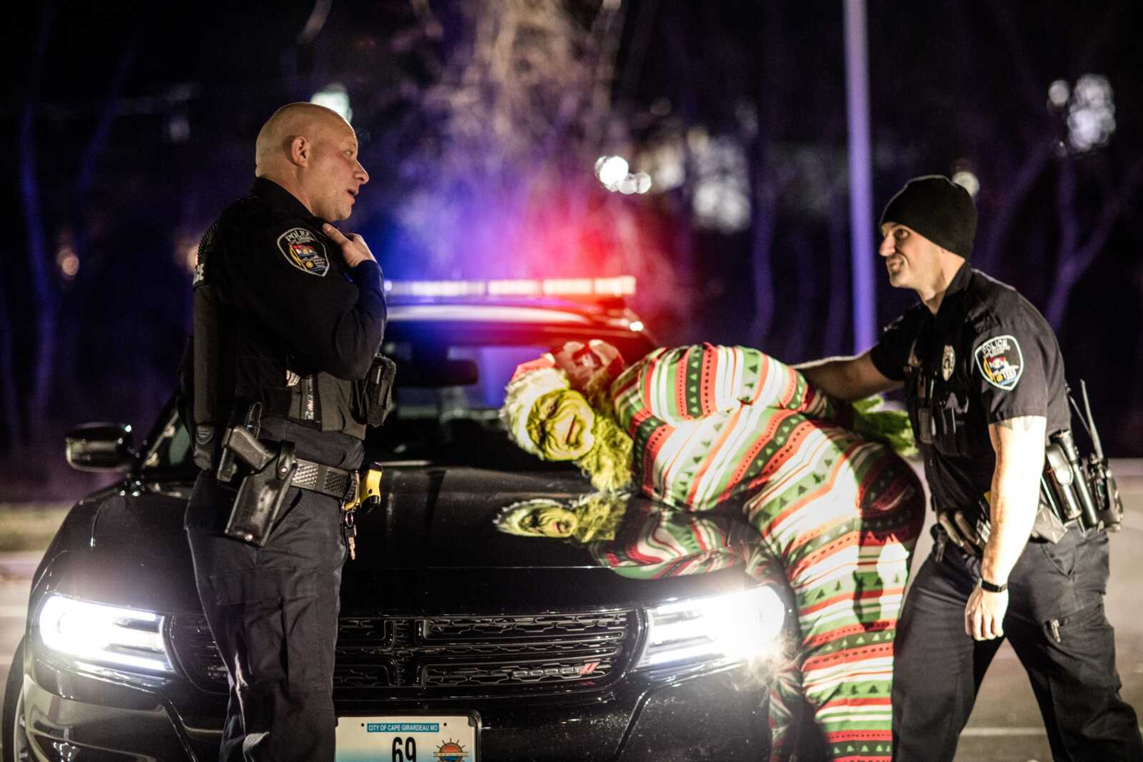 At the request of local photographer Ashley Irey, Cape Girardeau Police Department patrolmen Will Rogers, left, and Matthew Tisher, right, make a pretend arrest of Michael Irey, dressed as Dr. Seuss' the Grinch, on Sunday night near the police station in Cape Girardeau.