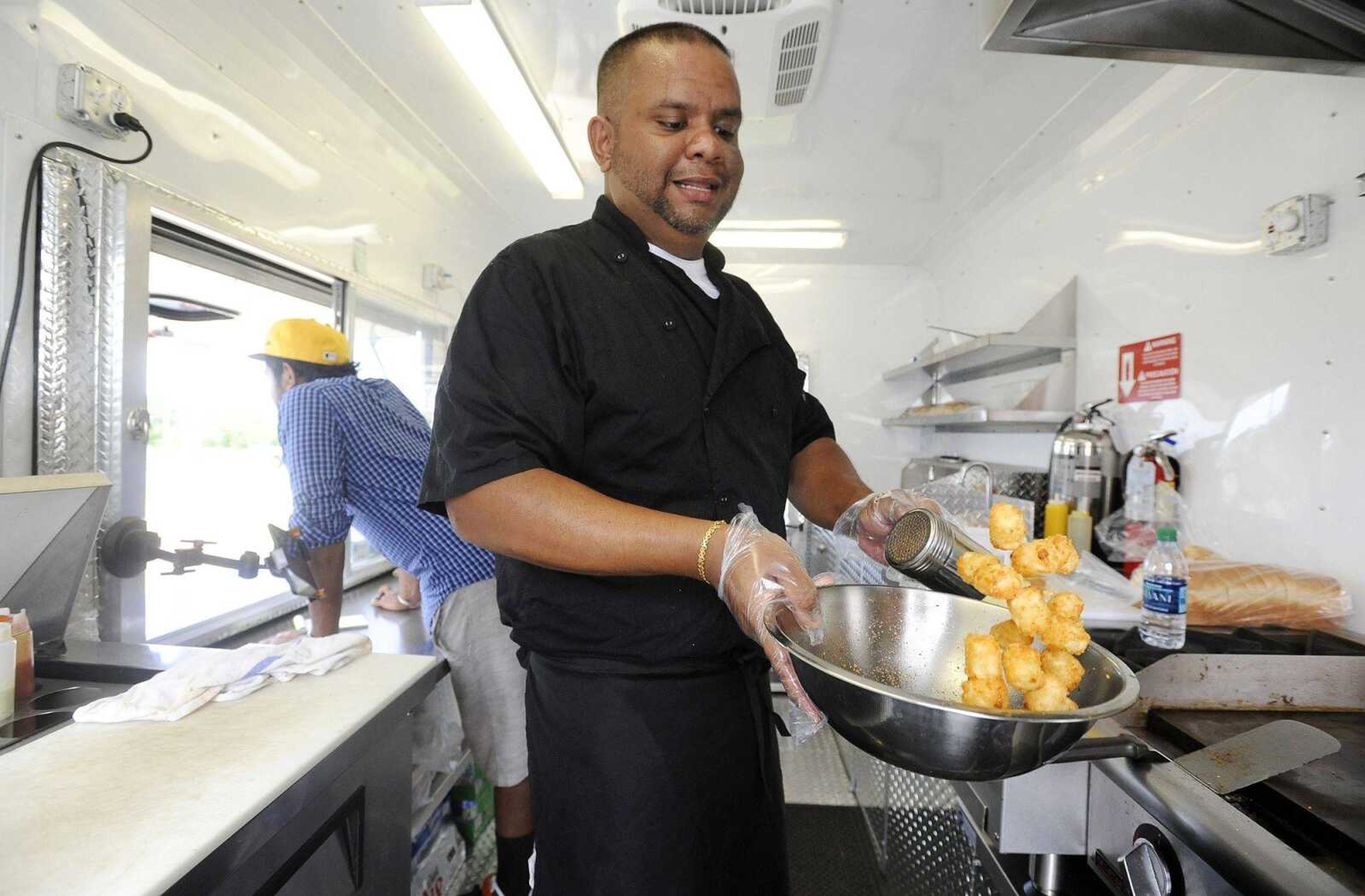 Amila Ramanayake seasons tater tots after taking them out of the frier Friday afternoon inside his food truck, the Melting Co., while it was parked at Plato's Closet in Cape GIrardeau.