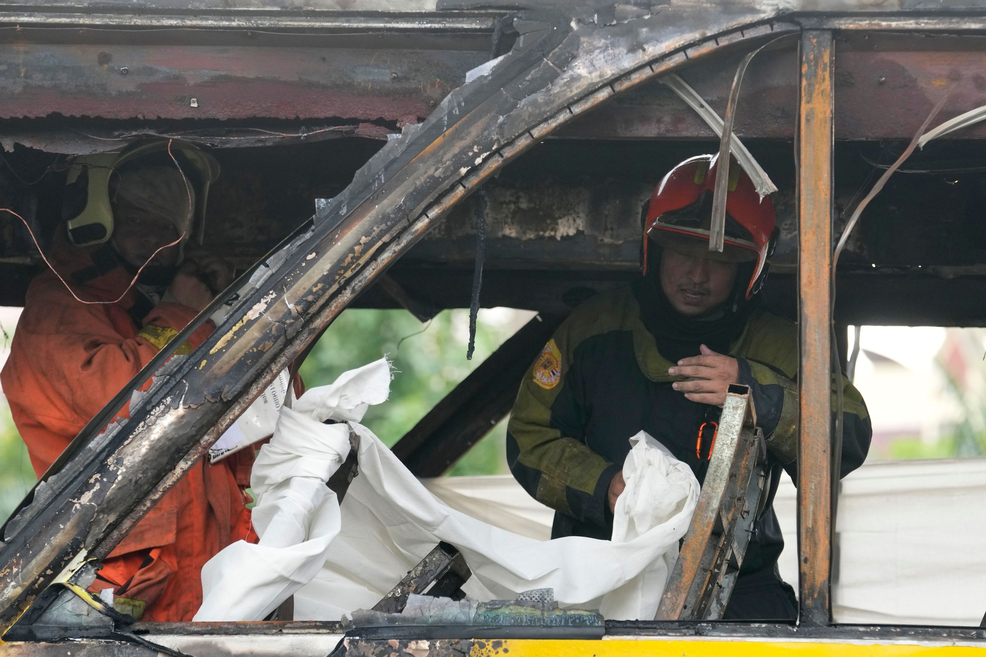 Rescuers hold a white cloth to cover the body of a victim inside a bus that caught fire, carrying young students with their teachers, in suburban Bangkok, Tuesday, Oct. 1, 2024. (AP Photo/Sakchai Lalit)