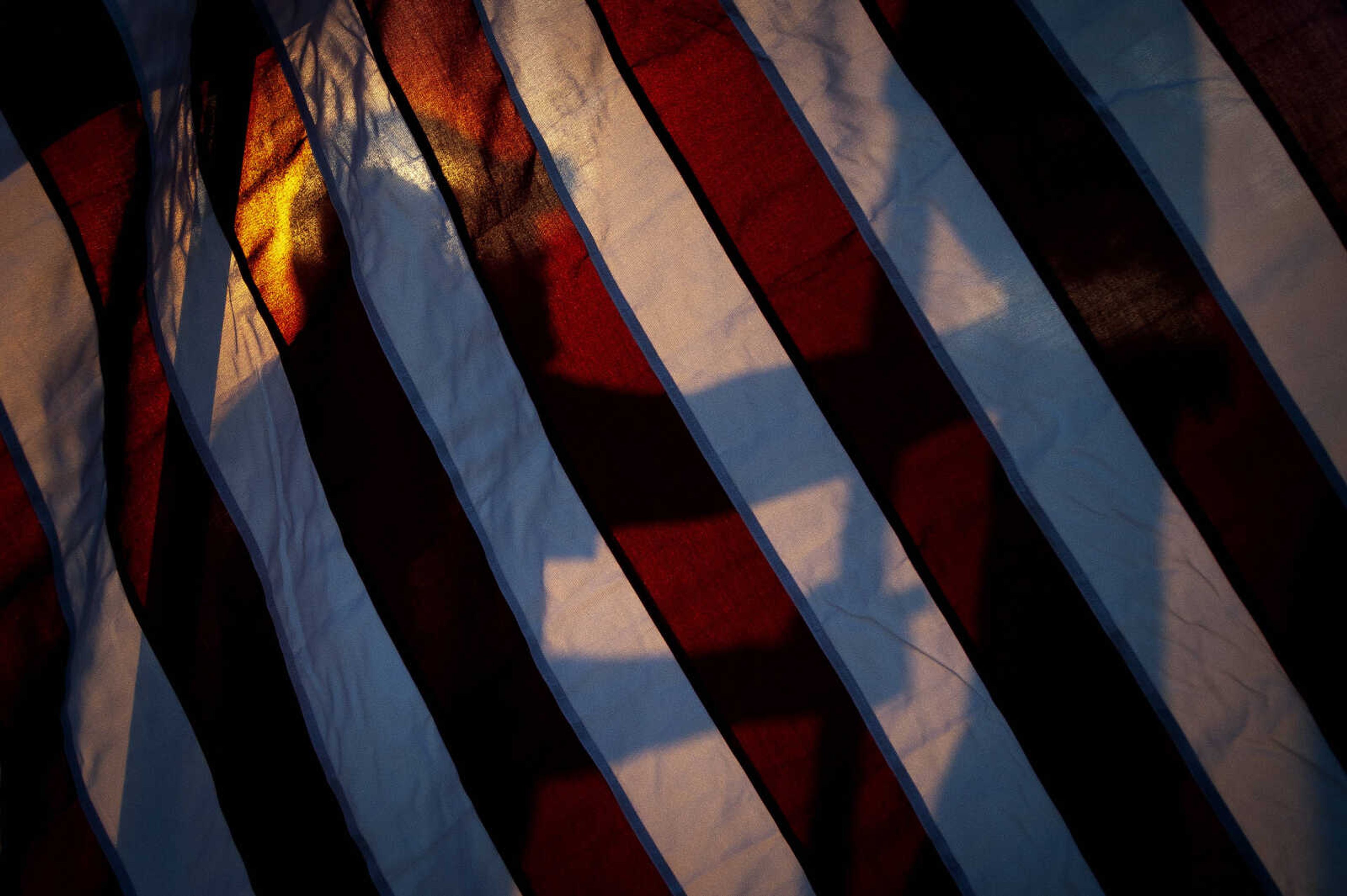 A helper is silhouetted through an American flag while assisting in assembling the Avenue of Flags for Patriot Day on Wednesday, Sept. 11, 2019, at Cape Girardeau County Park North in Cape Girardeau.