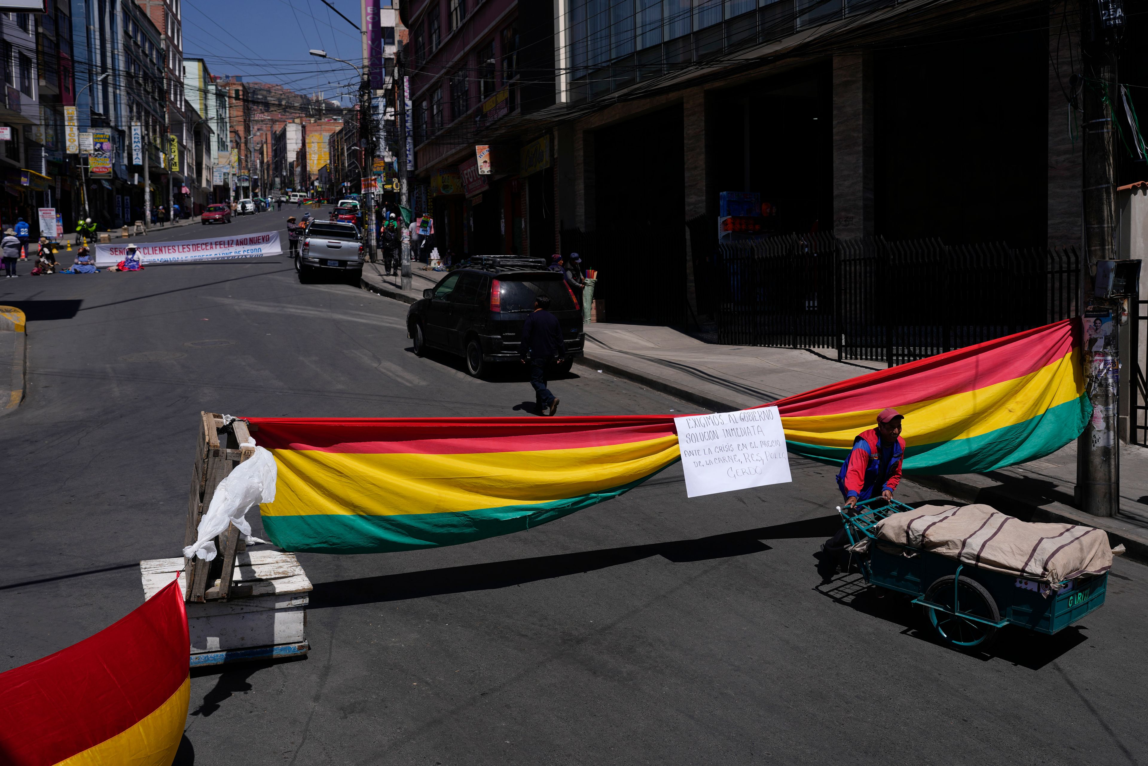 FILE - Meat vendors block a street with a Bolivian national flag near the market that they closed down for their 24-hour strike against inflation and to demand the government control border smuggling, in La Paz, Bolivia, Oct. 21, 2024. (AP Photo/Juan Karita)