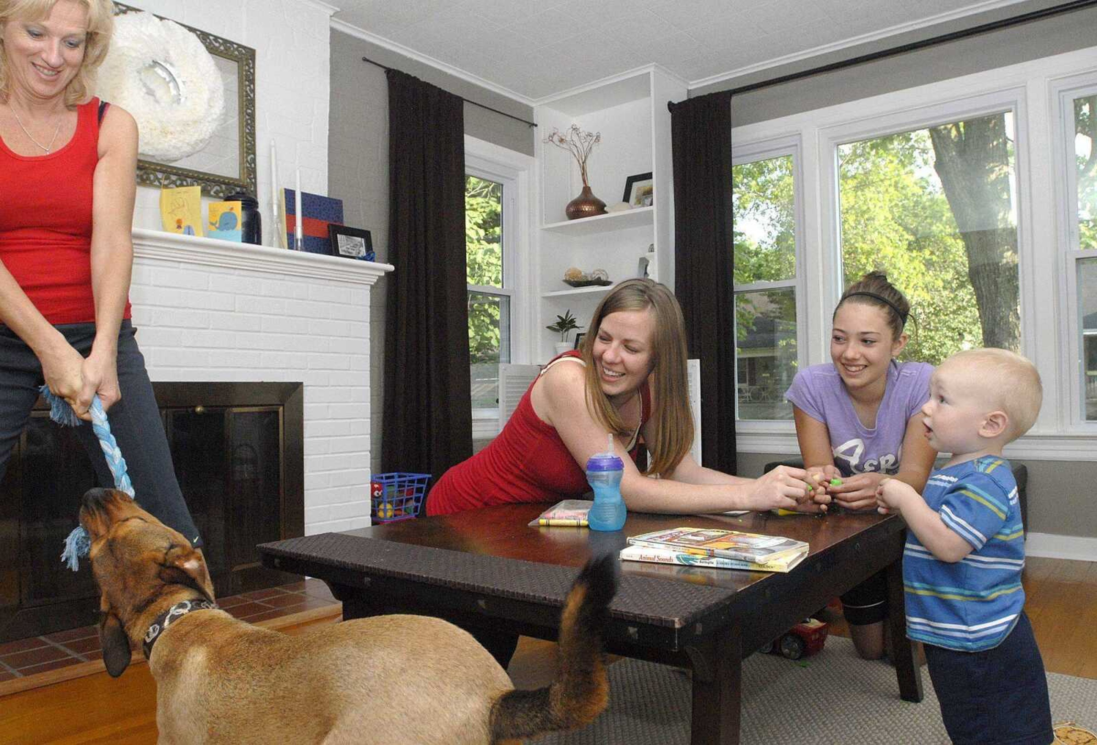 Kristal Flentge, second from left, her cousin Alexia Peal and son Isaac watch Flentge's mother Kathy Fish play tug-of-war Monday with their dog Butch in Cape Girardeau. Flentge and her husband, Chad, purchased this foreclosed home last year after returning to the area from St. Louis. (Laura Simon)