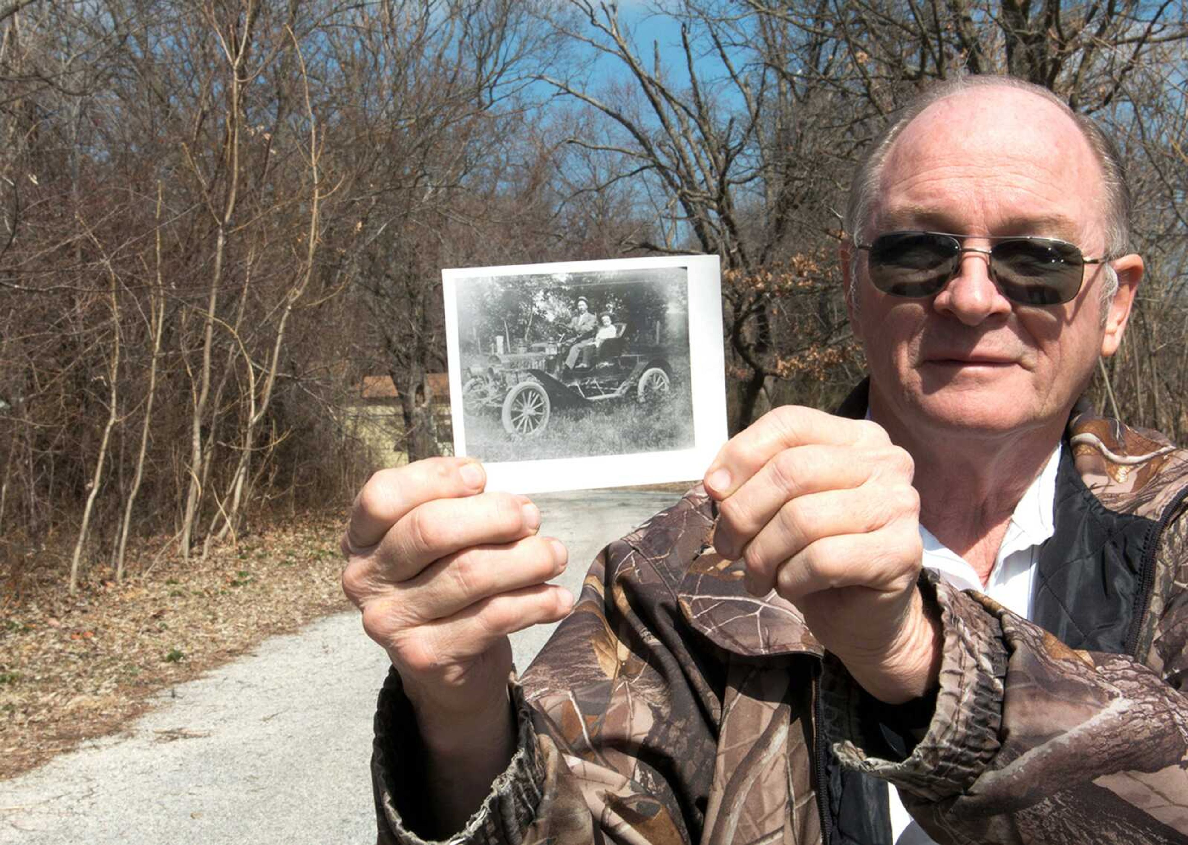 Gary Miller holds a photo of the third automobile in Neck City, Mo., belonging to Dr. W.G. Hogan as shown along a road now, March 19. (Roger Nomer ~ The Joplin Globe)