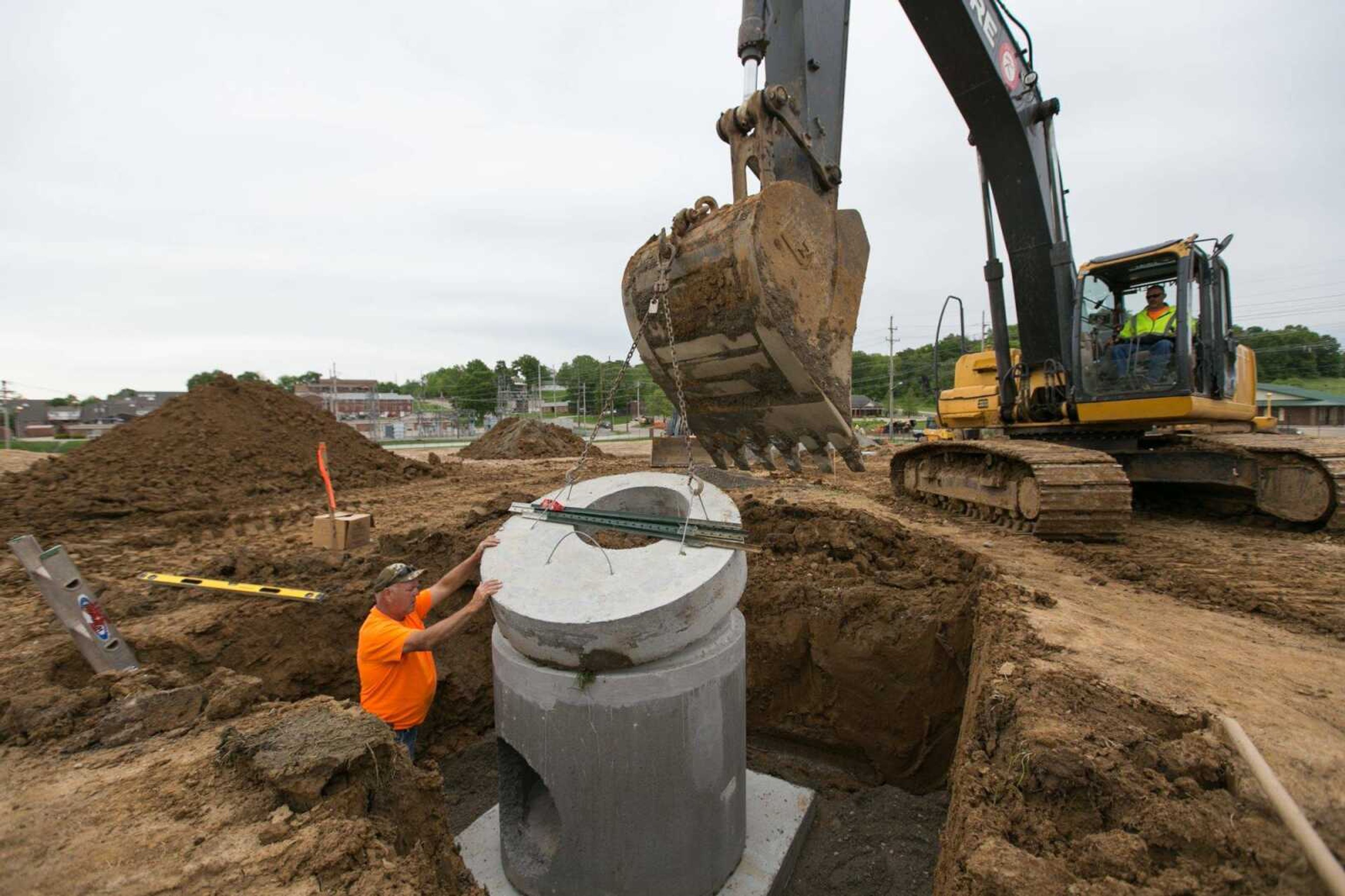 Paul Engelhart helps guide Jeff Sutton as he uses an excavator to lower a manhole cover into place Friday on the Chateau Girardeau campus.