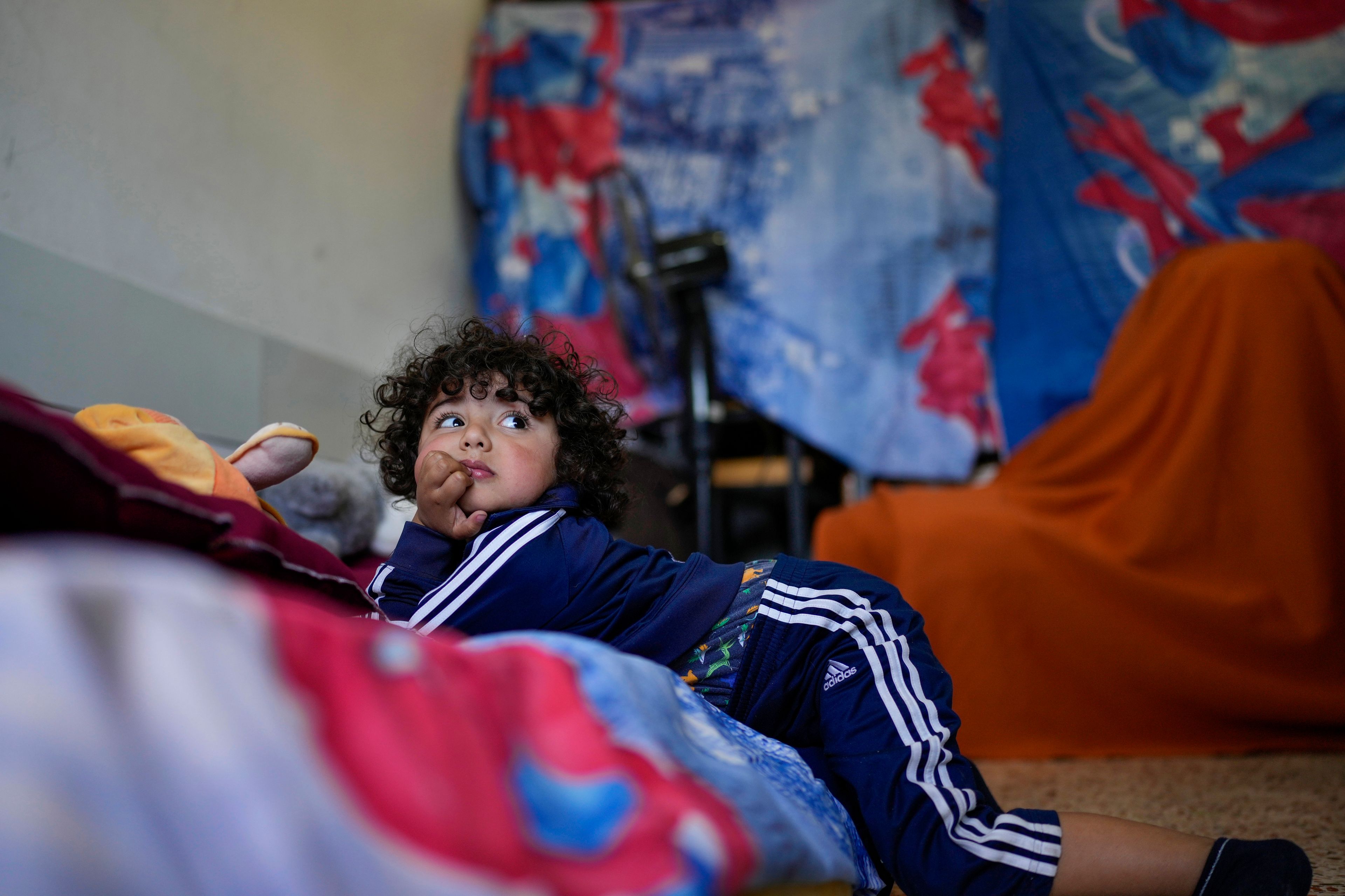 A displaced child who fled southern Lebanon with relatives during the ongoing Hezbollah-Israel war watches television inside a classroom in the village of Ebrine, northern Lebanon, Thursday, Oct. 24, 2024. (AP Photo/Hassan Ammar)