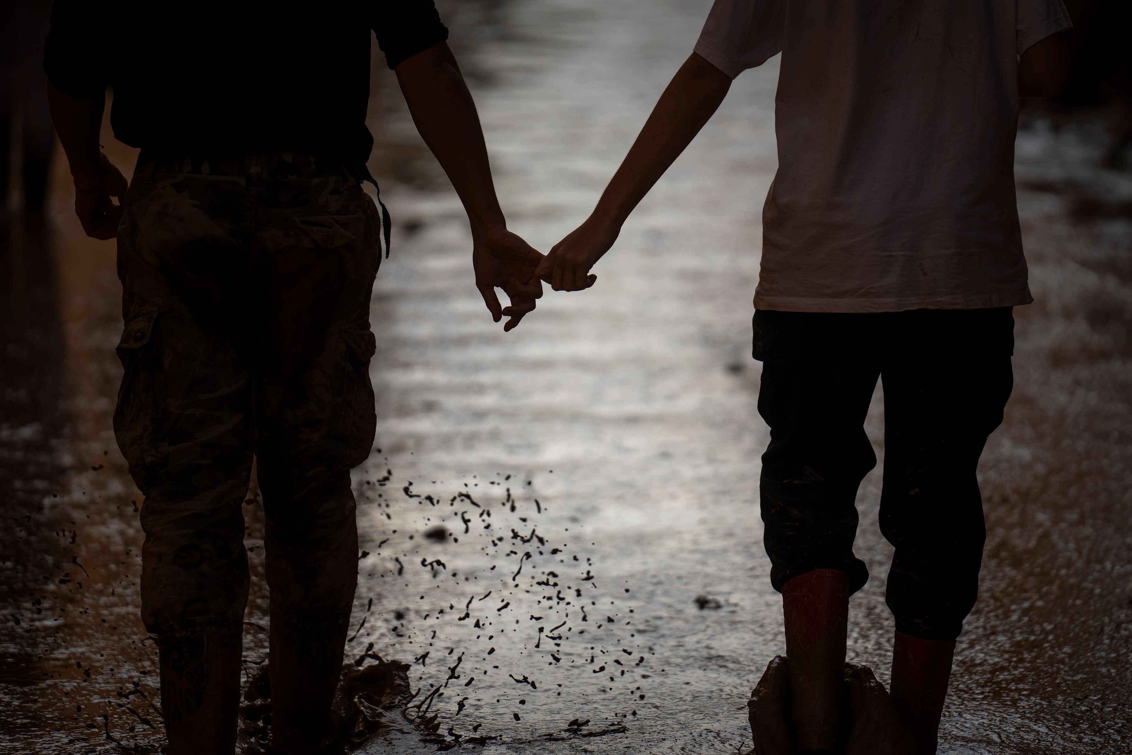 A couple of volunteers walk hand in hand down a muddy street in a flooded area in Masanasa, Valencia, Spain, Thursday, Nov. 7, 2024. (AP Photo/Emilio Morenatti)