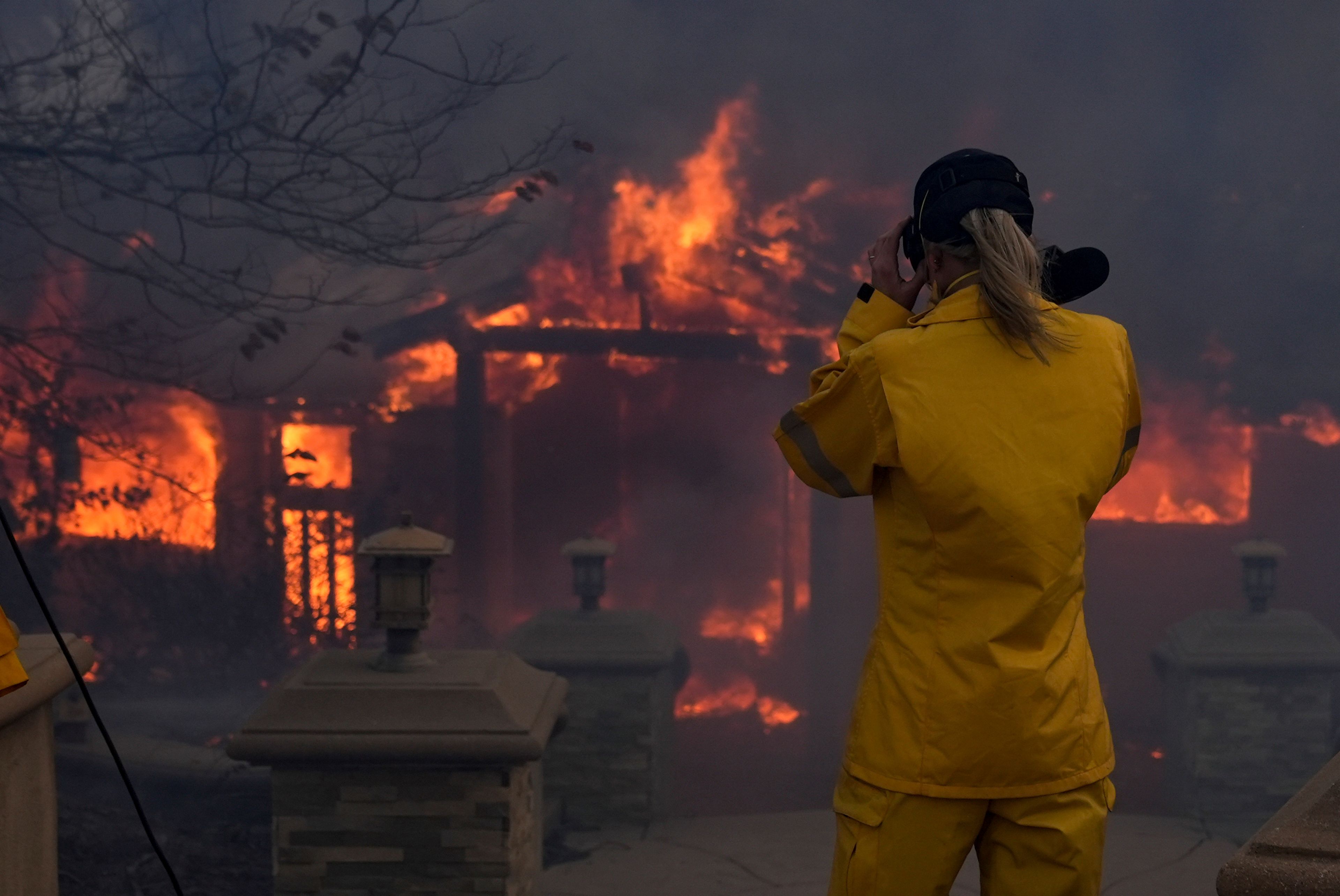 A television reporter stands in front of a burning home in the Mountain fire, Wednesday, Nov. 6, 2024, near Camarillo, Calif. (AP Photo/Marcio Jose Sanchez)