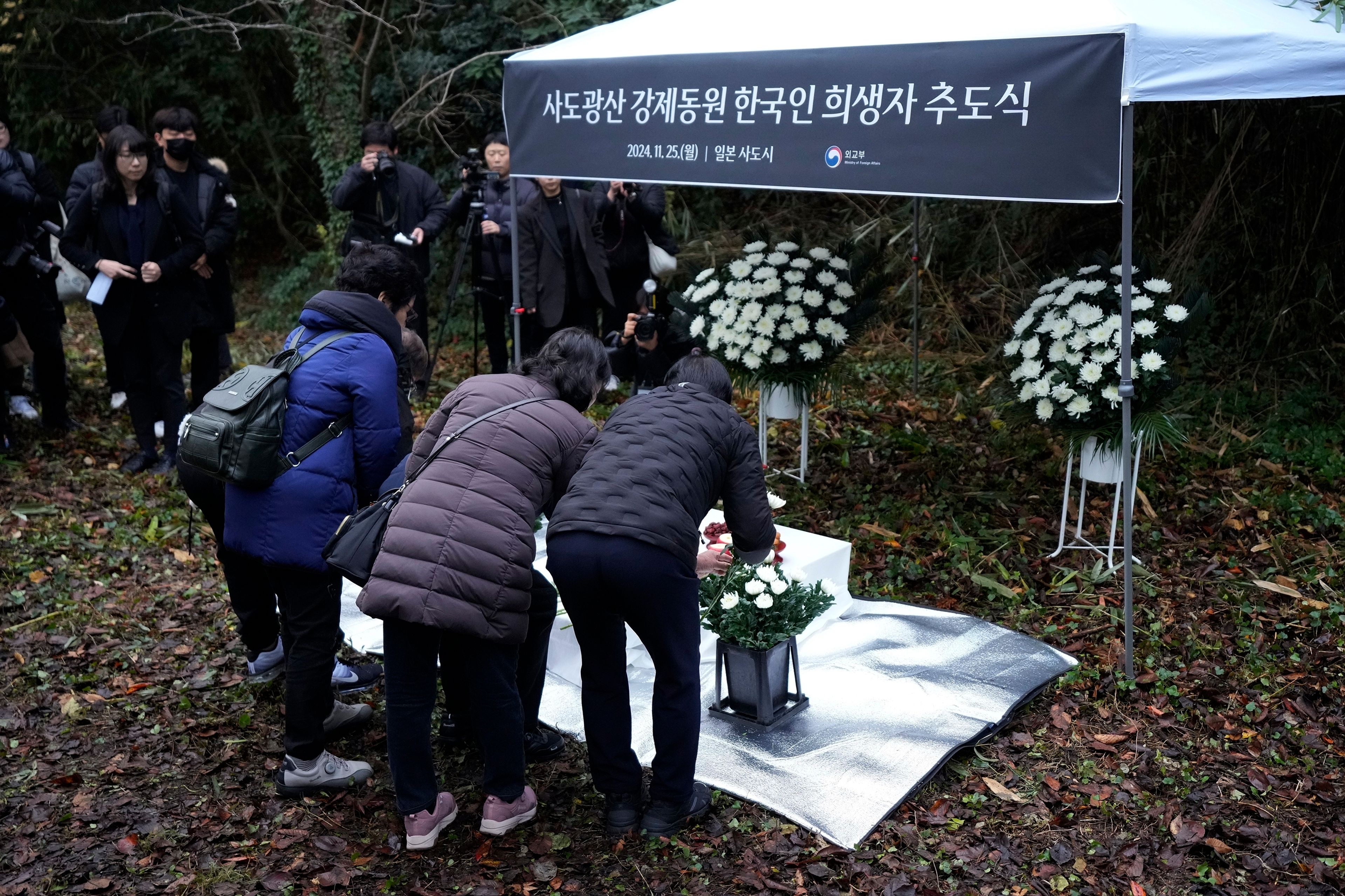 Relatives of Korean victims and South Korean officials offer flowers during a memorial service in Sado, Niigata prefecture, Japan, Monday, Nov. 25, 2024, after boycotting a memorial organized by Japanese officials. The black banner reads " A memorial service for Korean forced laborer victims at Sado Mine." (AP Photo/Eugene Hoshiko)