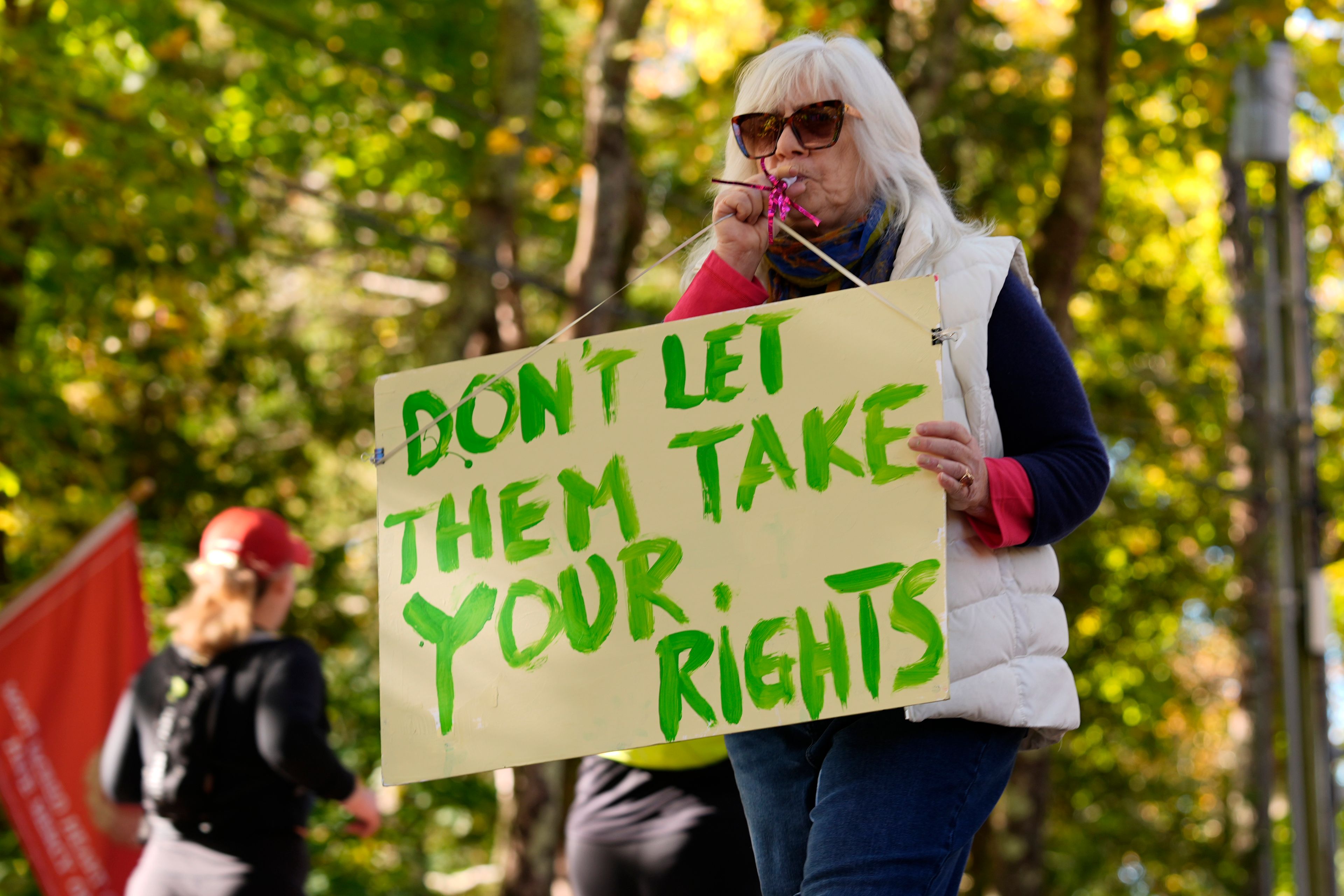 Susan Buell protests in front of the home of Leonard Leo during the Mount Desert Island Marathon, Sunday, Oct. 20, 2024, in Northeast Harbor, Maine. (AP Photo/Robert F. Bukaty)