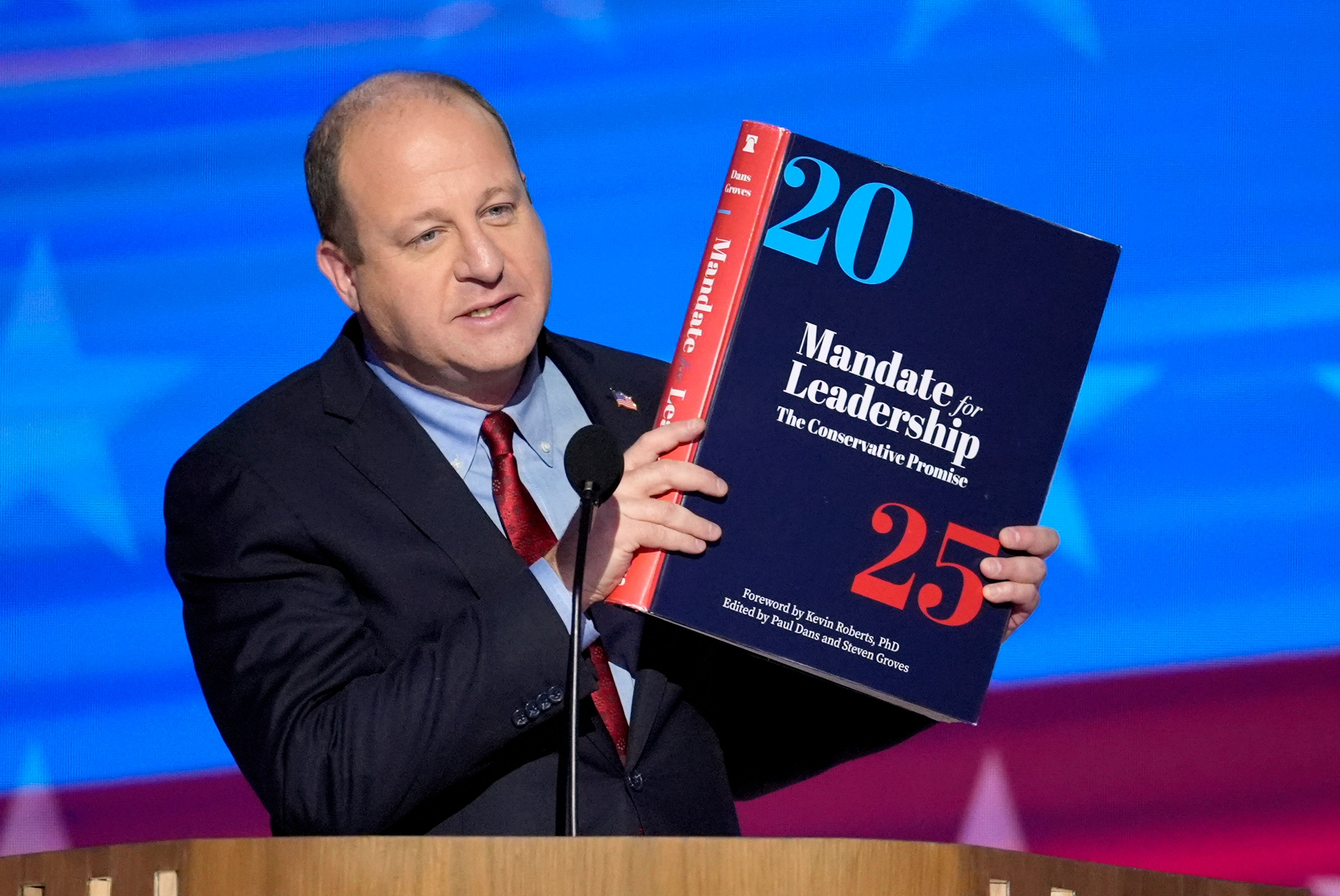 FILE - Colorado Gov. Jared Polis holds up a copy of Project 2025 as he speaks during the Democratic National Convention Aug. 21, 2024, in Chicago. (AP Photo/J. Scott Applewhite, File)