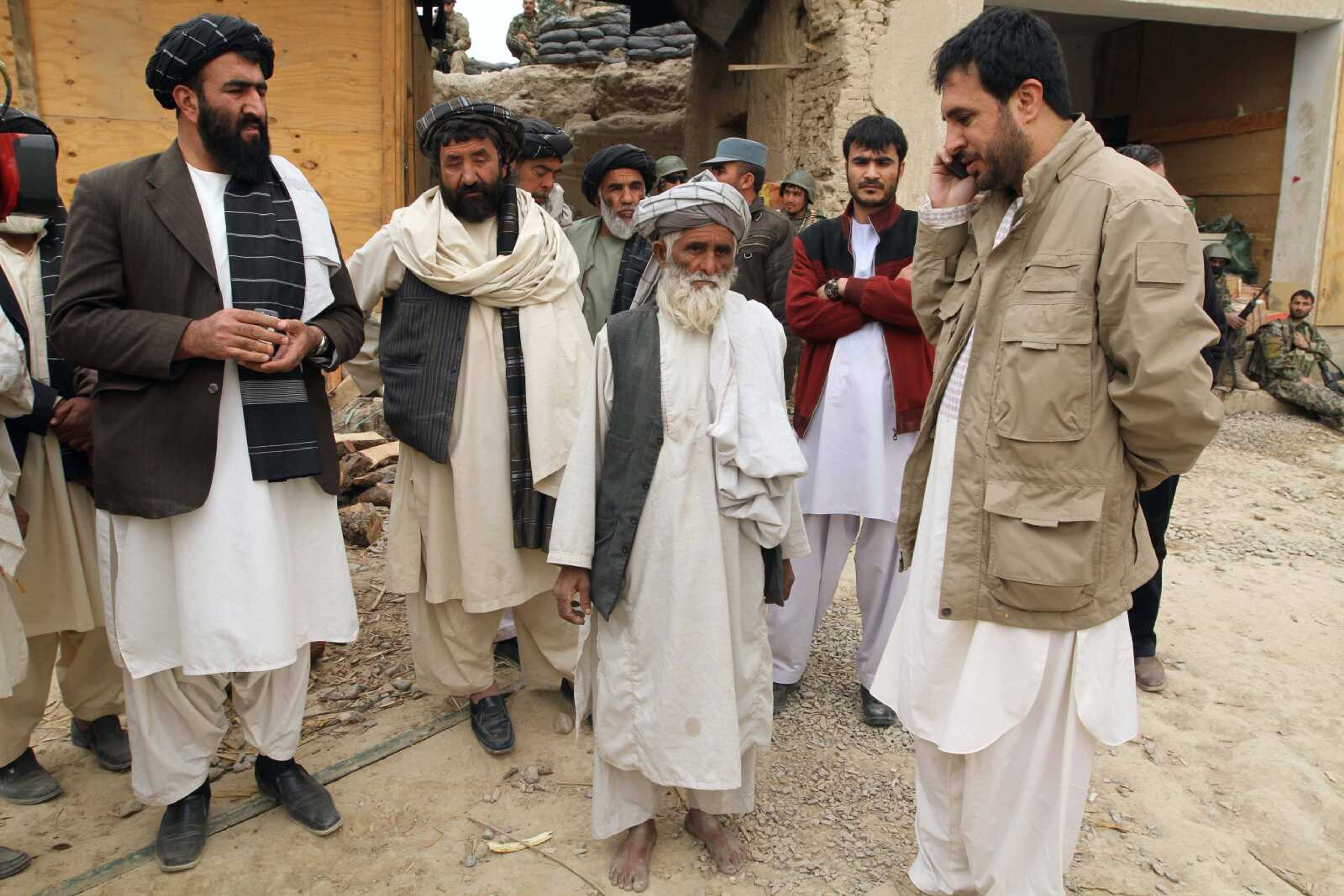 In this Sunday, March 11, 2012 photo, Afghan official Asadullah Khaled, right, makes a phone call as villagers gather at a U.S. military base after the death of 16 civilians in Panjwai, Kandahar province south of Kabul, Afghanistan, Sunday, March 11, 2012. At centre is Abdul Samad who is reported to have lost several members of his family in the incident. An Afghan youth recounted on Monday the terrifying scene in his home as a lone U.S. soldier moved stealthily through it during a killing spree, then crouched down and shot his father in the thigh as he stepped out of the bedroom. The soldier, now in U.S. custody, is accused of killing 16 Afghan civilians in their homes in the middle of the night between Saturday and Sunday and then burning some of their corpses. Afghan President Hamid Karzai said nine of those killed were children and three were women.(AP Photo/Allauddin Khan)