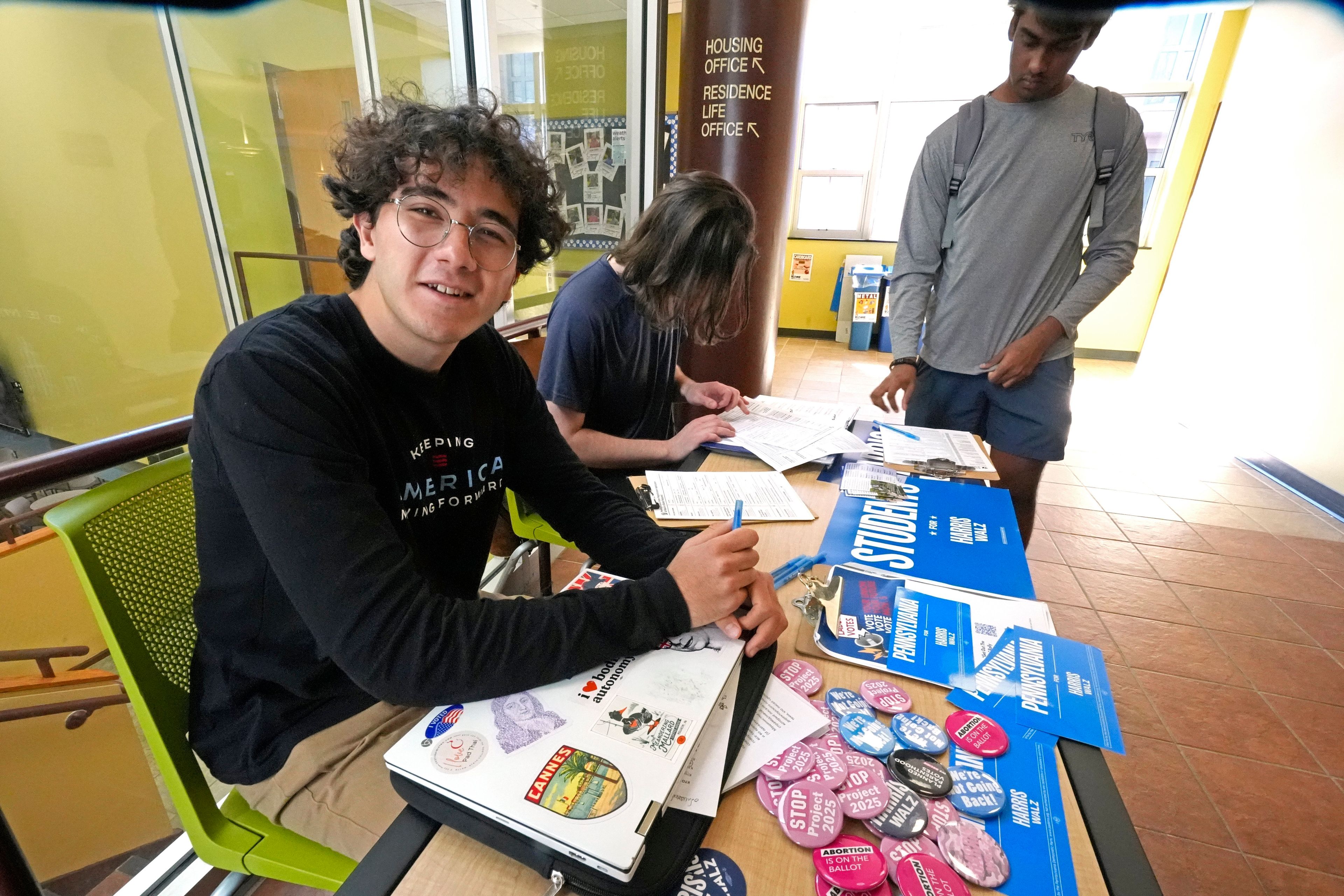 Penn State students Baybars Charkas, left, of Lancaster, Pa., and James Wachtman, center, of Swarthmore, Pa., man a voter registration table on the Penn State campus in University Park, Pa., Friday, Oct. 18, 2024. (AP Photo/Gene J. Puskar)