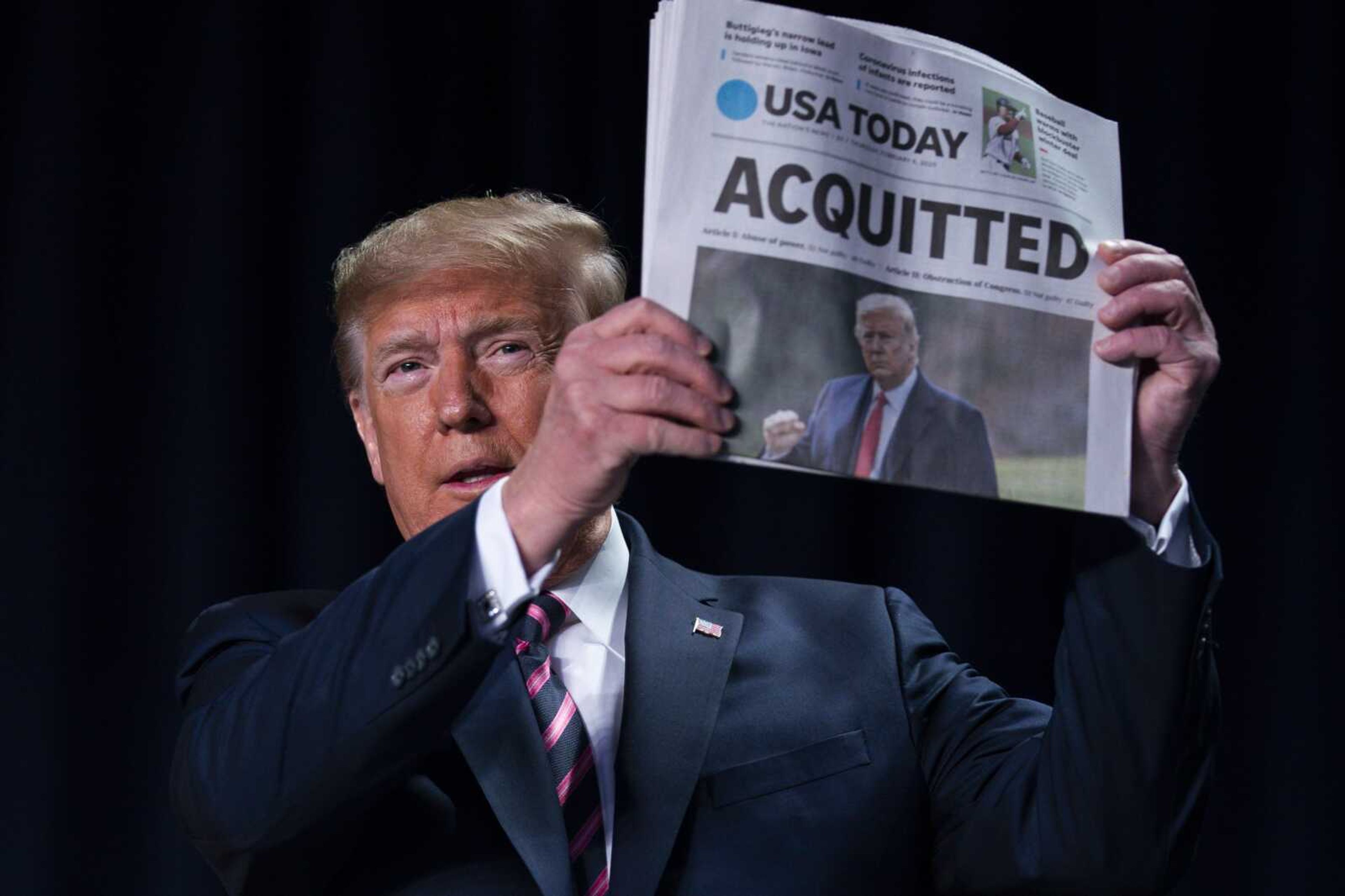 President Donald Trump holds up a newspaper with the headline that reads "ACQUITTED" at the 68th annual National Prayer Breakfast on Thursday in Washington.