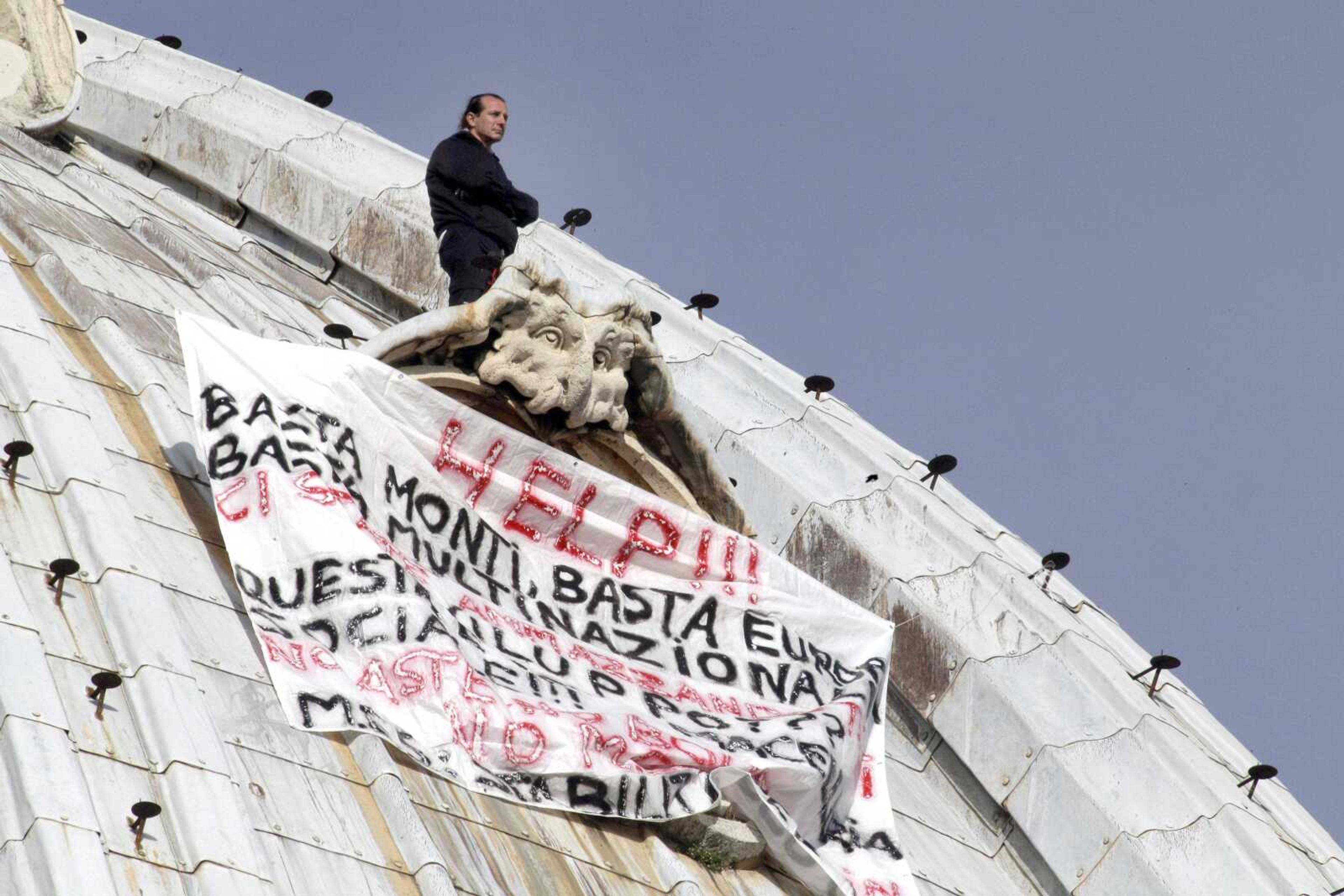 Italian businessman Marcello di Finizio stands above his banner, which reads in Italian, &#8220;Help!! Enough Monti [Italian Premier Mario Monti], enough Europe, enough multinationals, you are killing all of us. Development?? This is a social butchery!!&#8221;, as he protests Wednesday on St. Peter&#8217;s Basilica&#8217;s 42-feet-high dome at the Vatican. (Andrew Medichini ~ Associated Press)