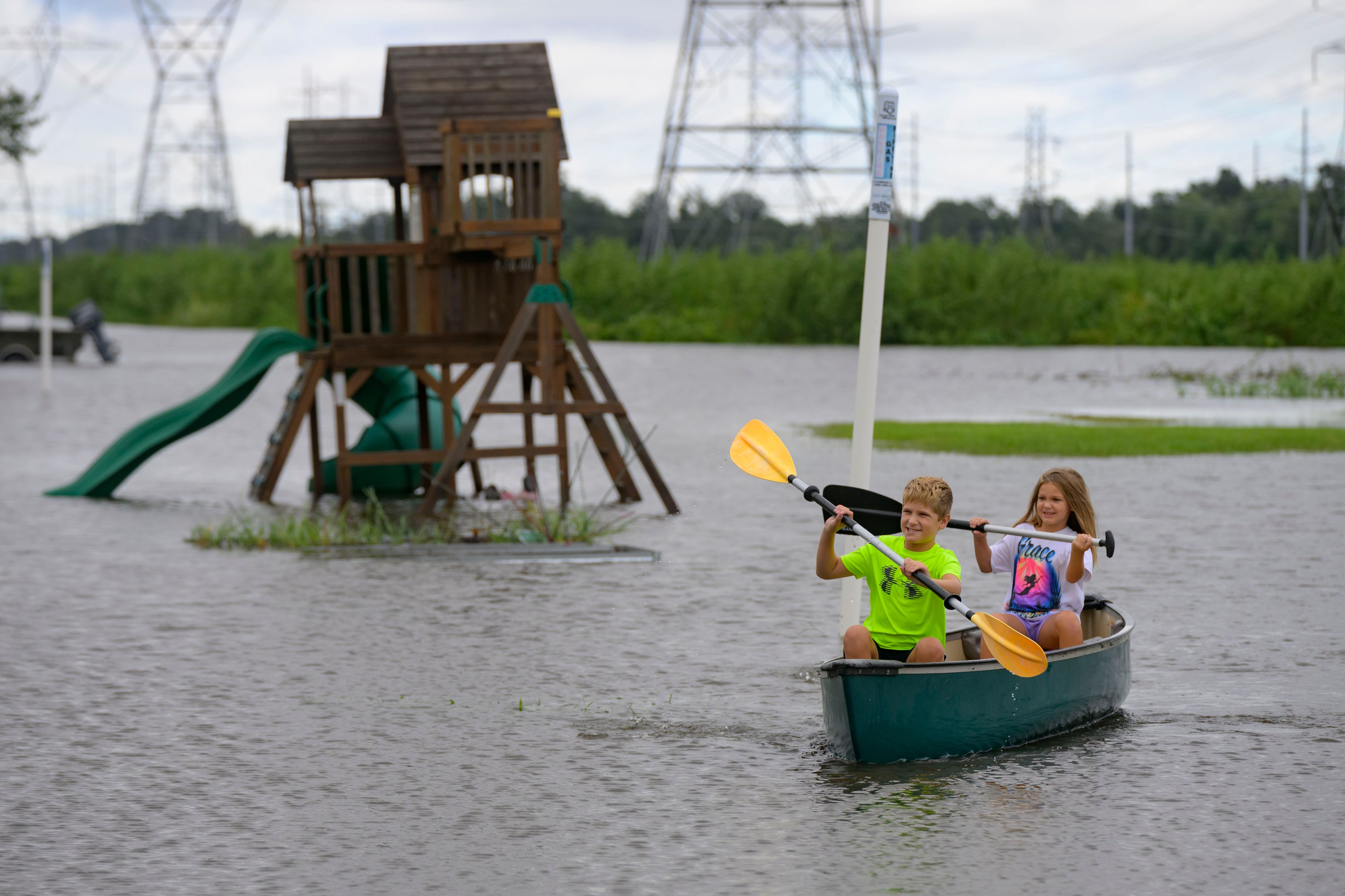 Siblings Avery, 10, and Grace LeBlanc, 7, canoe in their backyard next to playground equipment after flooding from Hurricane Francine in Montz, La., in St. Charles Parish, Thursday, Sept. 12, 2024. (AP Photo/Matthew Hinton)