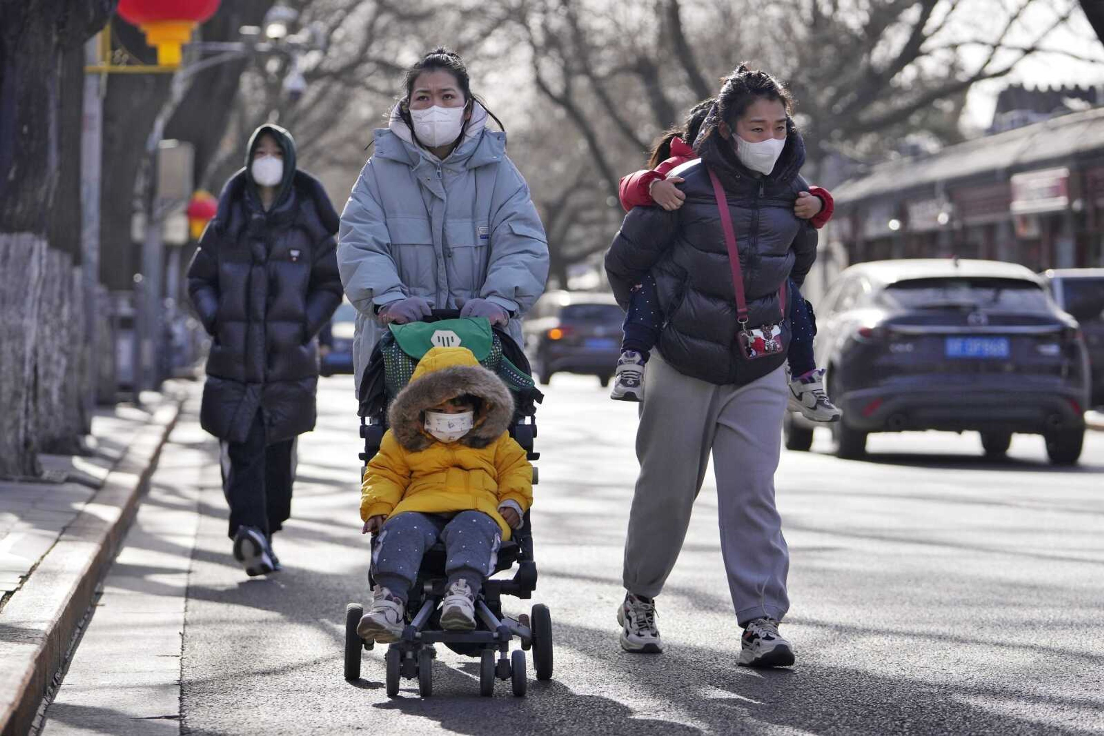 Women wearing face masks walk with their children on a street Tuesday as they head to Forbidden City in Beijing. China has announced its first population decline in decades as what has been the world's most populous nation ages and its birthrate plunges.