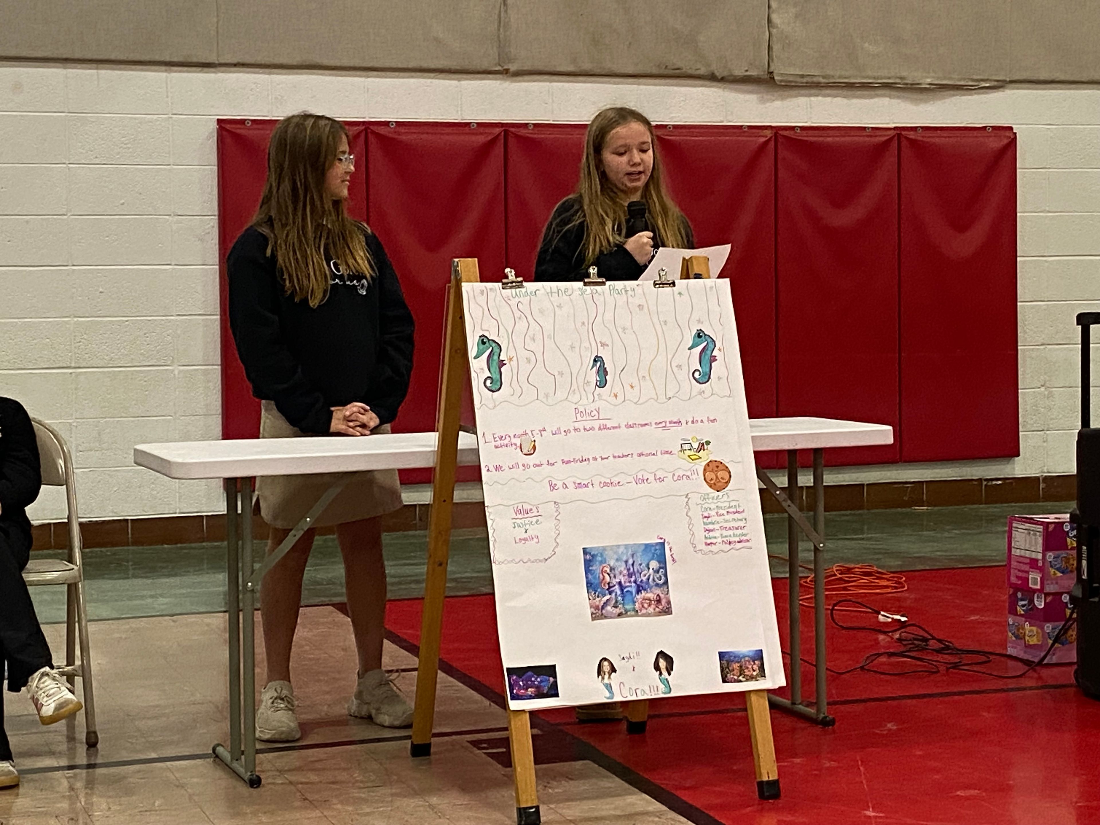 Cora Houchins, presidential candidate for the "Under the Sea Party" answers the debate question as her vice-presidential running mate, Saydi Priggel, stands by.