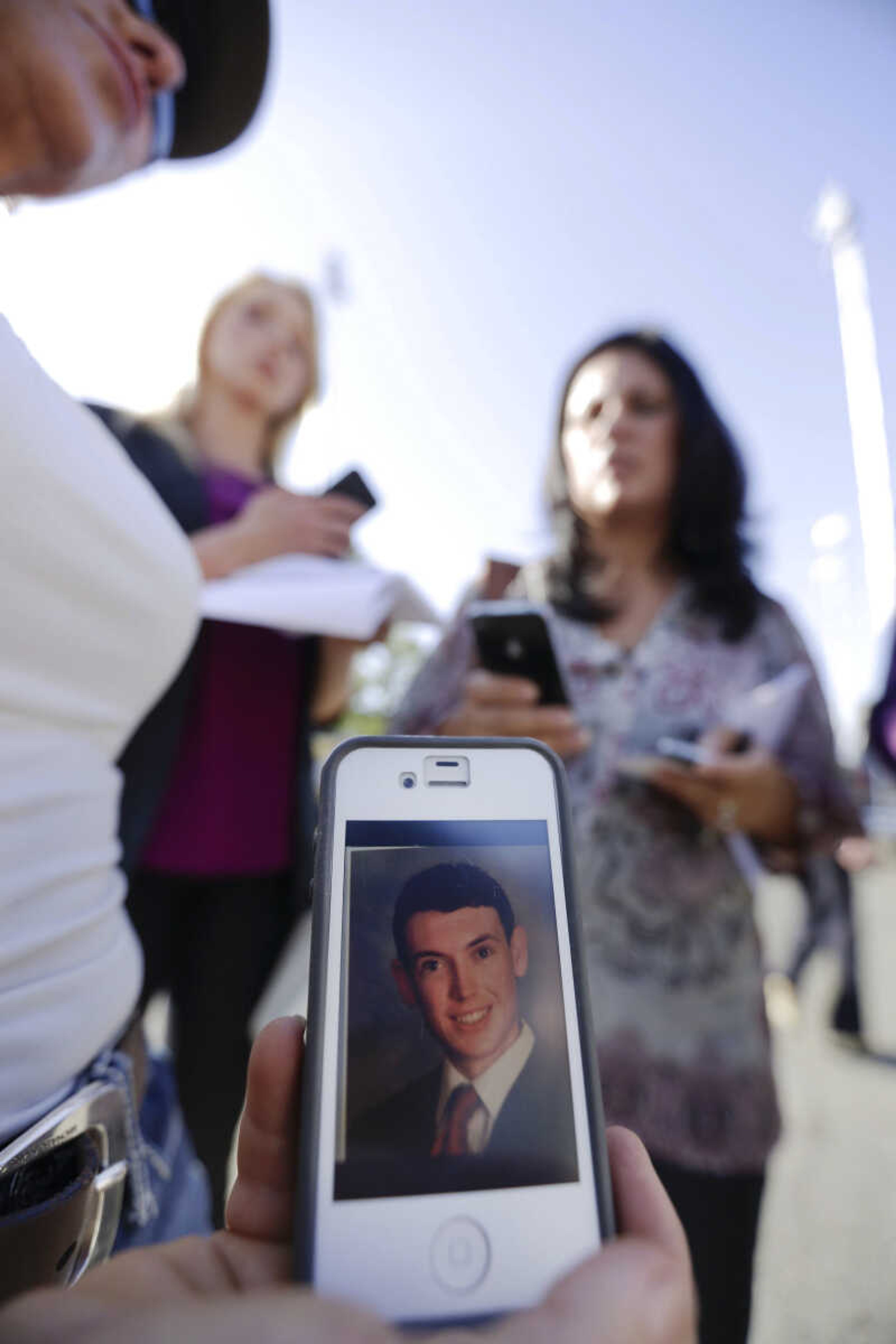 Julie Adams, left, holds her phone displaying a 2006 Westview High School yearbook picture of Colorado shooting suspect James Holmes in front of the Holmes family house in San Diego on Friday, July 20, 2012. Adams, a neighbor of his parents, said she did not know James Holmes. A gunman in a gas mask barged into a crowded Denver-area theater during a midnight showing of the Batman movie on Friday, hurled a gas canister and then opened fire in one of the deadliest mass shootings in recent U.S. history. (AP Photo/Gregory Bull)