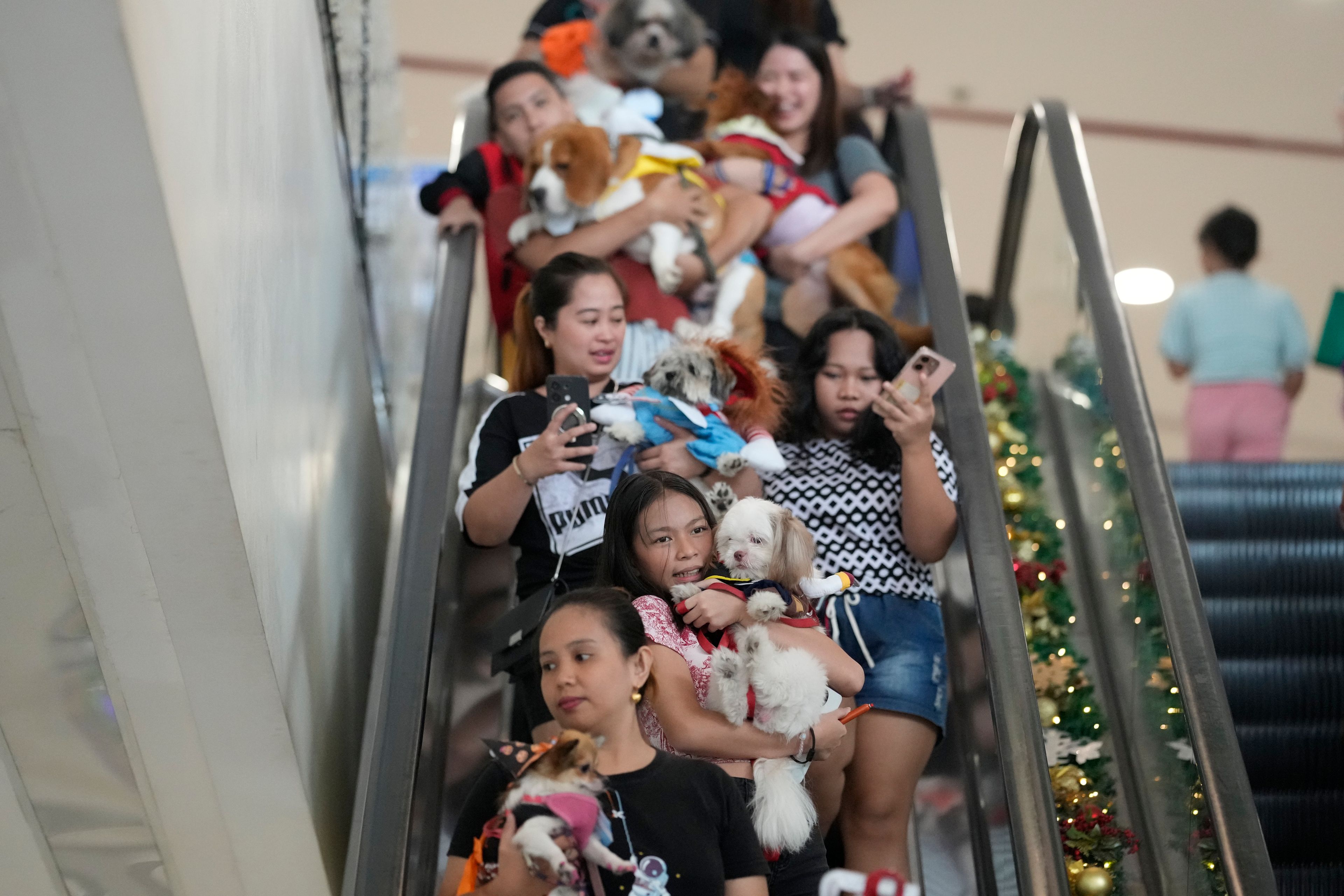 Owners carry their dogs in costumes down an escalator during a Halloween pet party at a mall in Valenzuela city, Philippines on Saturday, Oct. 19, 2024. (AP Photo/Aaron Favila)