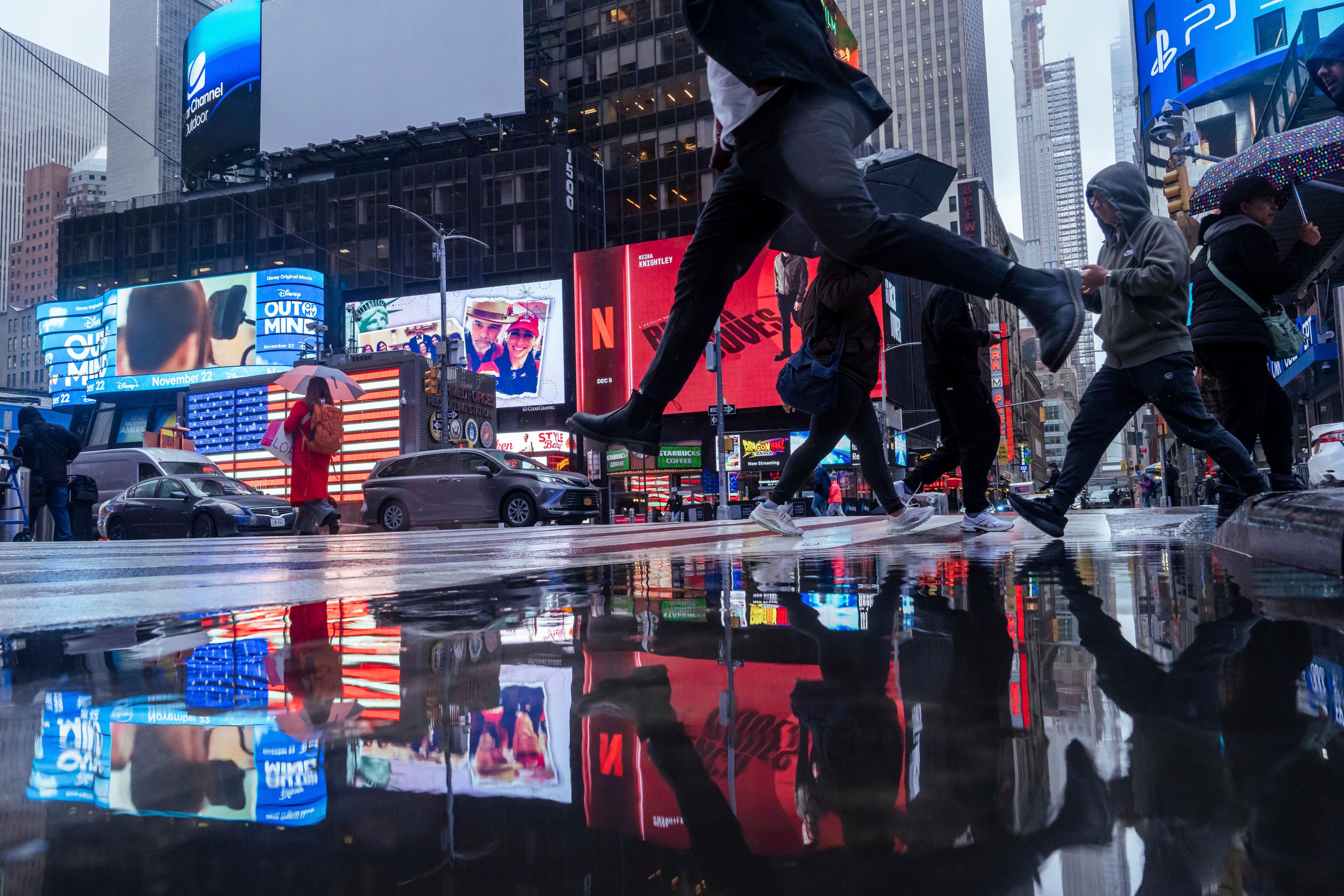 A person jumps over a rain puddle as people cross the street in Times Square, Thursday, Nov. 21, 2024, in New York. (AP Photo/Adam Gray)