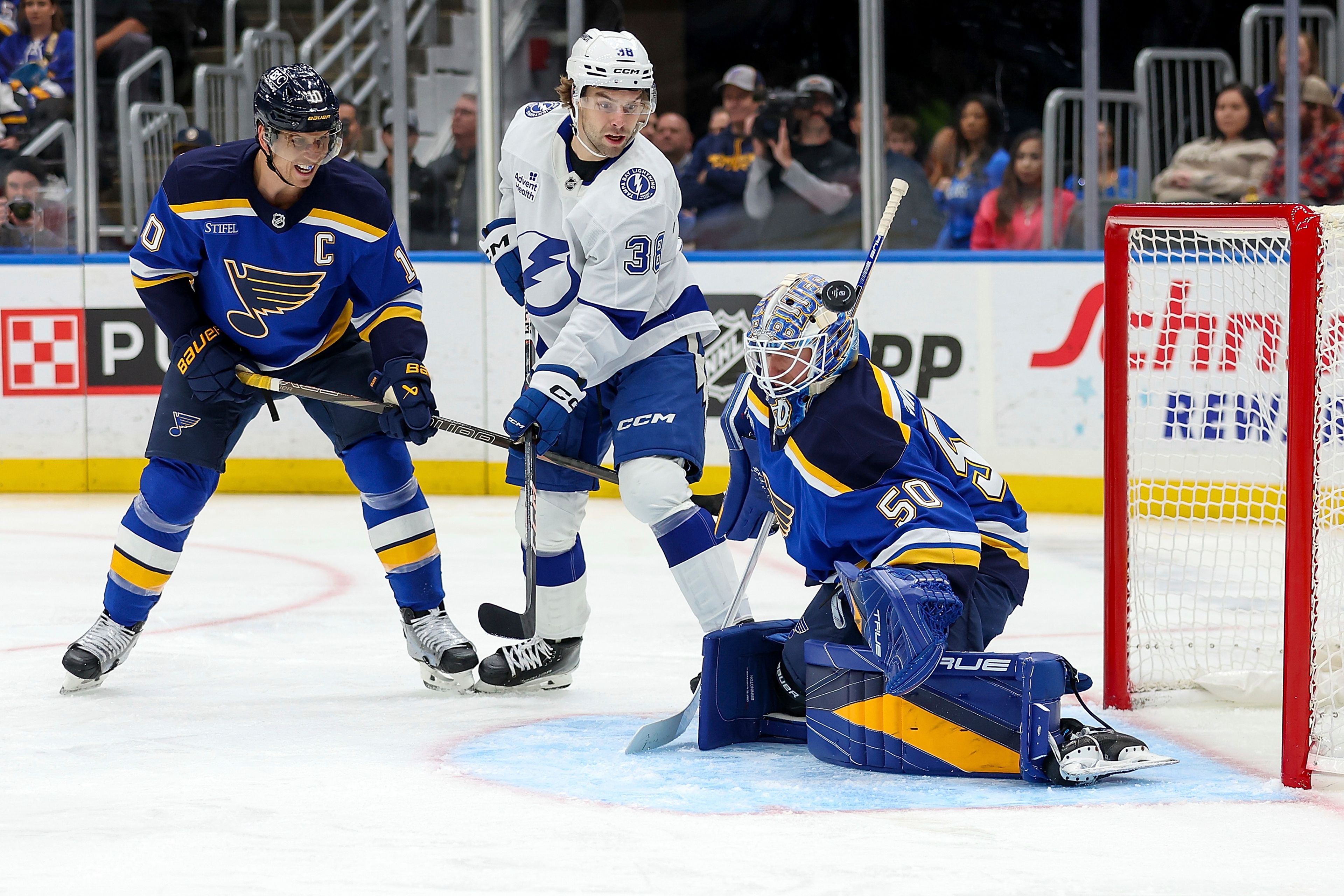 St. Louis Blues' Brayden Schenn (10) and Tampa Bay Lightning's Brandon Hagel (38) watch as the puck is deflected by St. Louis Blues goaltender Jordan Binnington (50) during the first period of an NHL hockey game Tuesday, Nov. 5, 2024, in St. Louis. (AP Photo/Scott Kane)