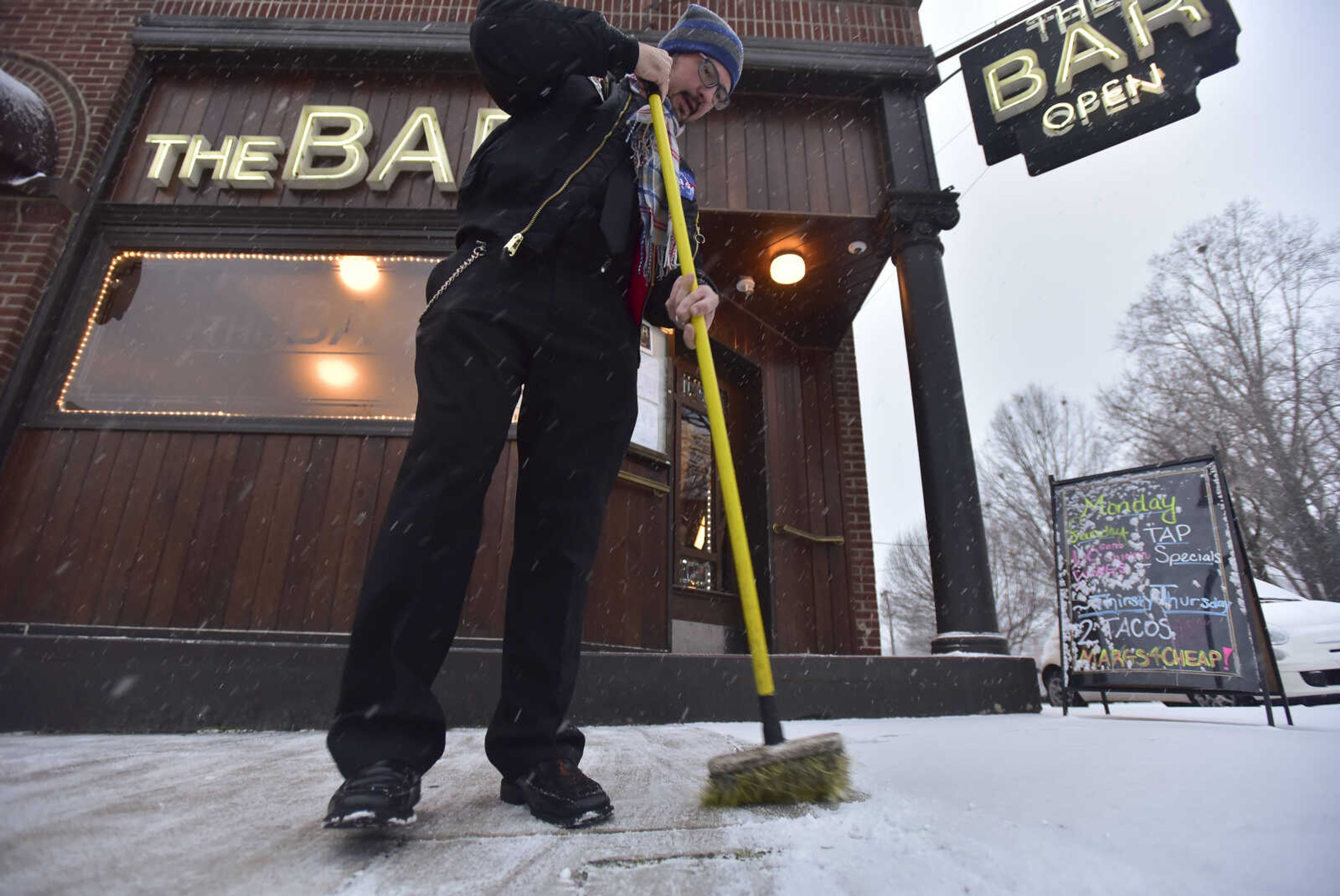 Matthew Hendricks, the General Manager for The Bar, sweeps away snow before it sticks to the ground Thursday, Jan. 5, 2016 in Cape Girardeau.