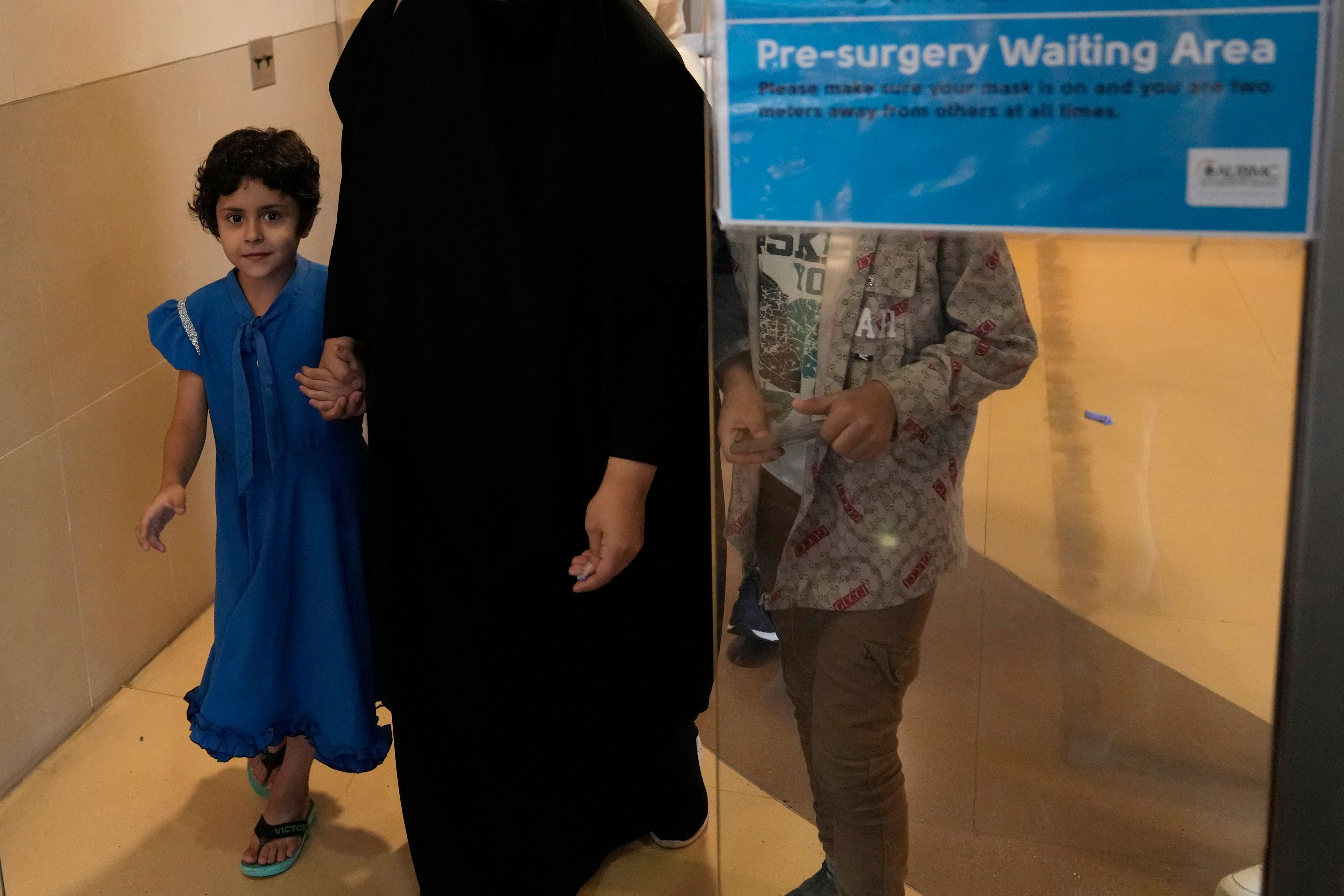 Halima Abou Yassine, 7, who was brought to Lebanon from Gaza for treatment after an Israeli strike left her near death with a gaping wound in her skull, walks with her mother ahead of surgery at the American University of Beirut Medical Center, in Beirut, Lebanon, Monday, July 15, 2024. (AP Photo/Hussein Malla)