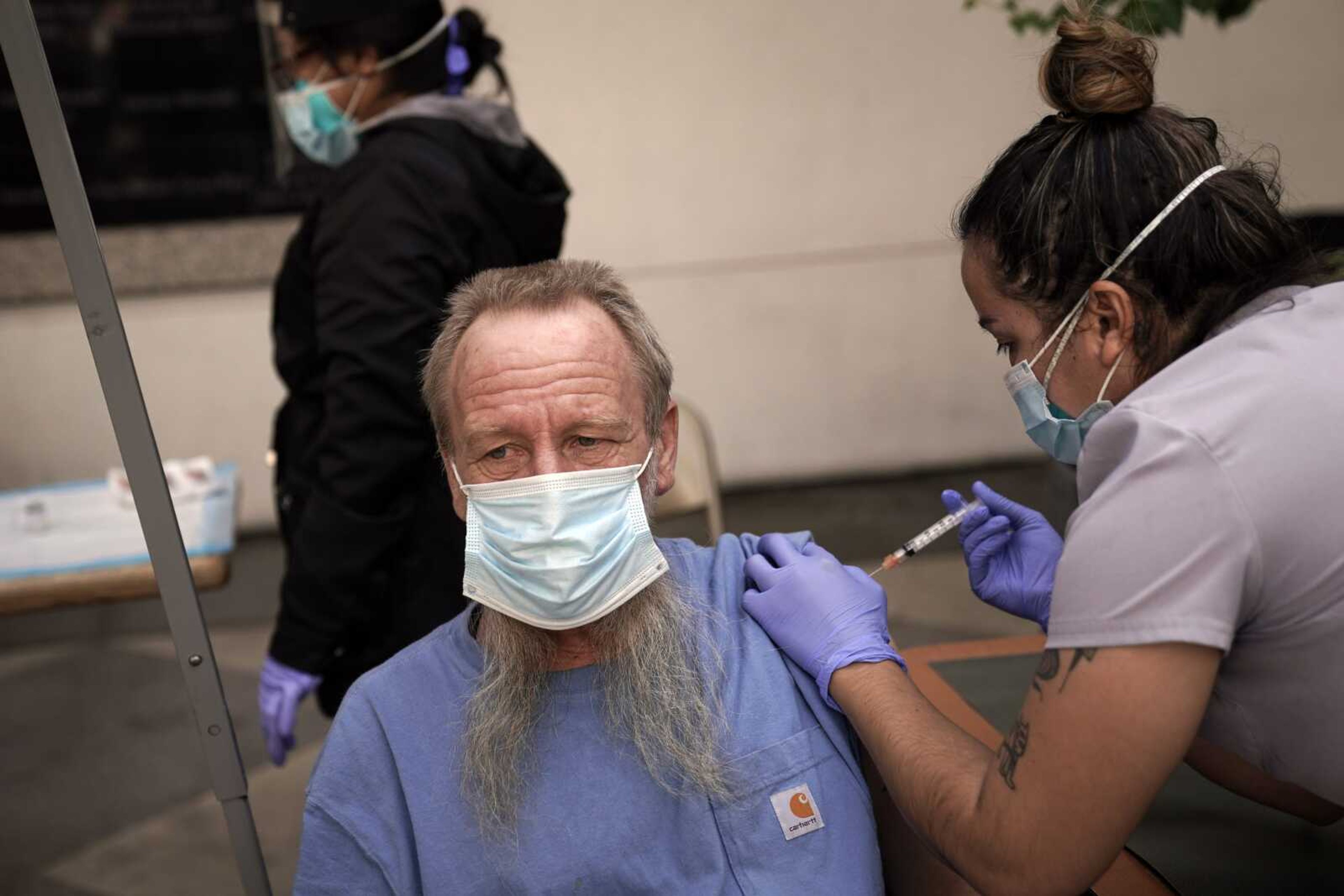 EMT Rachel Bryant, right, administers a COVID-19 vaccine to a homeless man in the courtyard of the Midnight Mission on Feb. 3 in Los Angeles.