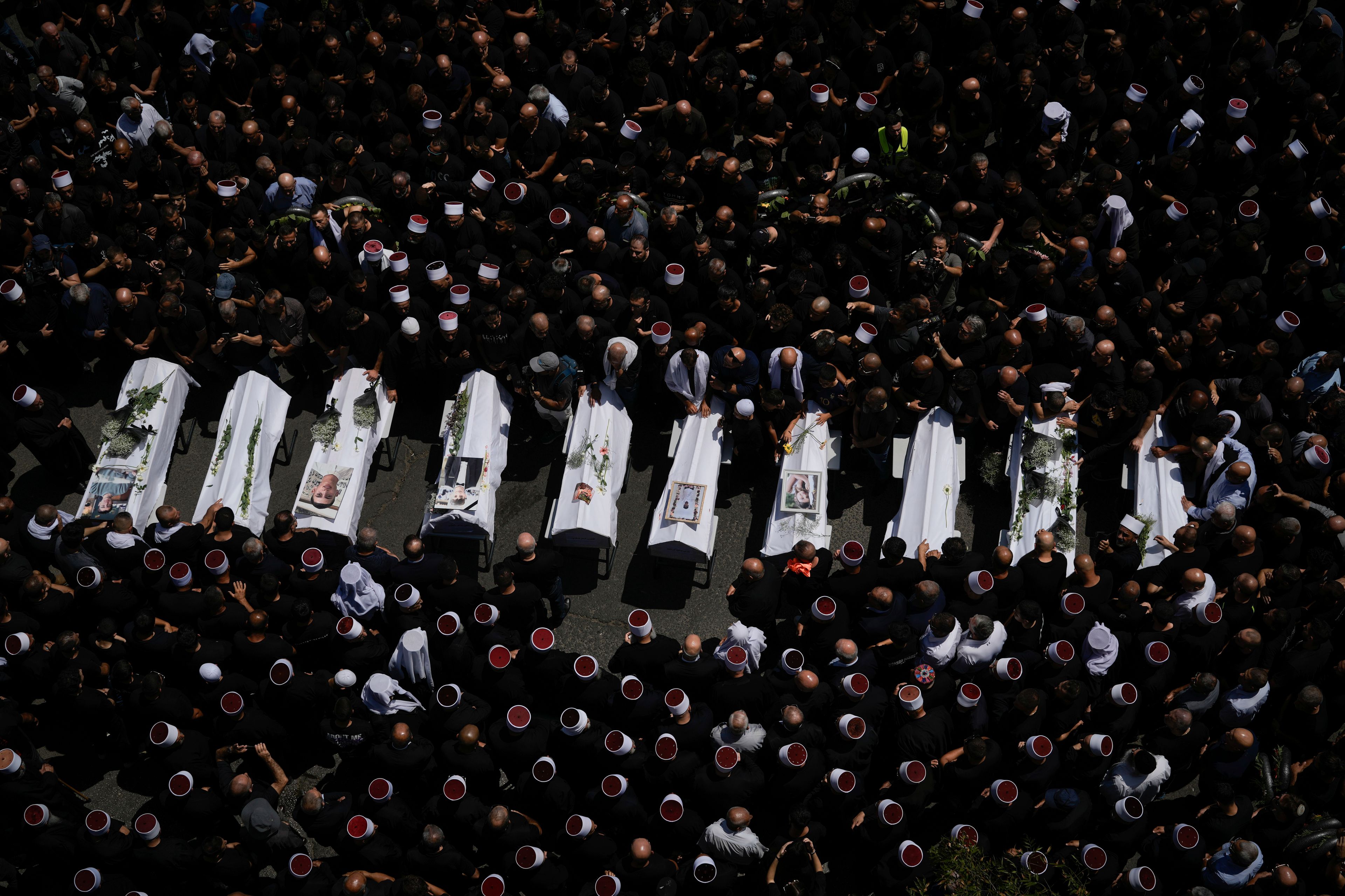 Mourners from the Druze minority surround the bodies of some of the 12 children and teens killed in a rocket strike at a soccer field, in the village of Majdal Shams at the Israeli-controlled Golan Heights, Sunday, July 28, 2024. A rocket strike at a soccer field in the village has killed at least 12 children and teens. It's the deadliest strike on an Israeli target along the country's northern border since the fighting between Israel and the Lebanese militant group Hezbollah began. (AP Photo/Leo Correa)