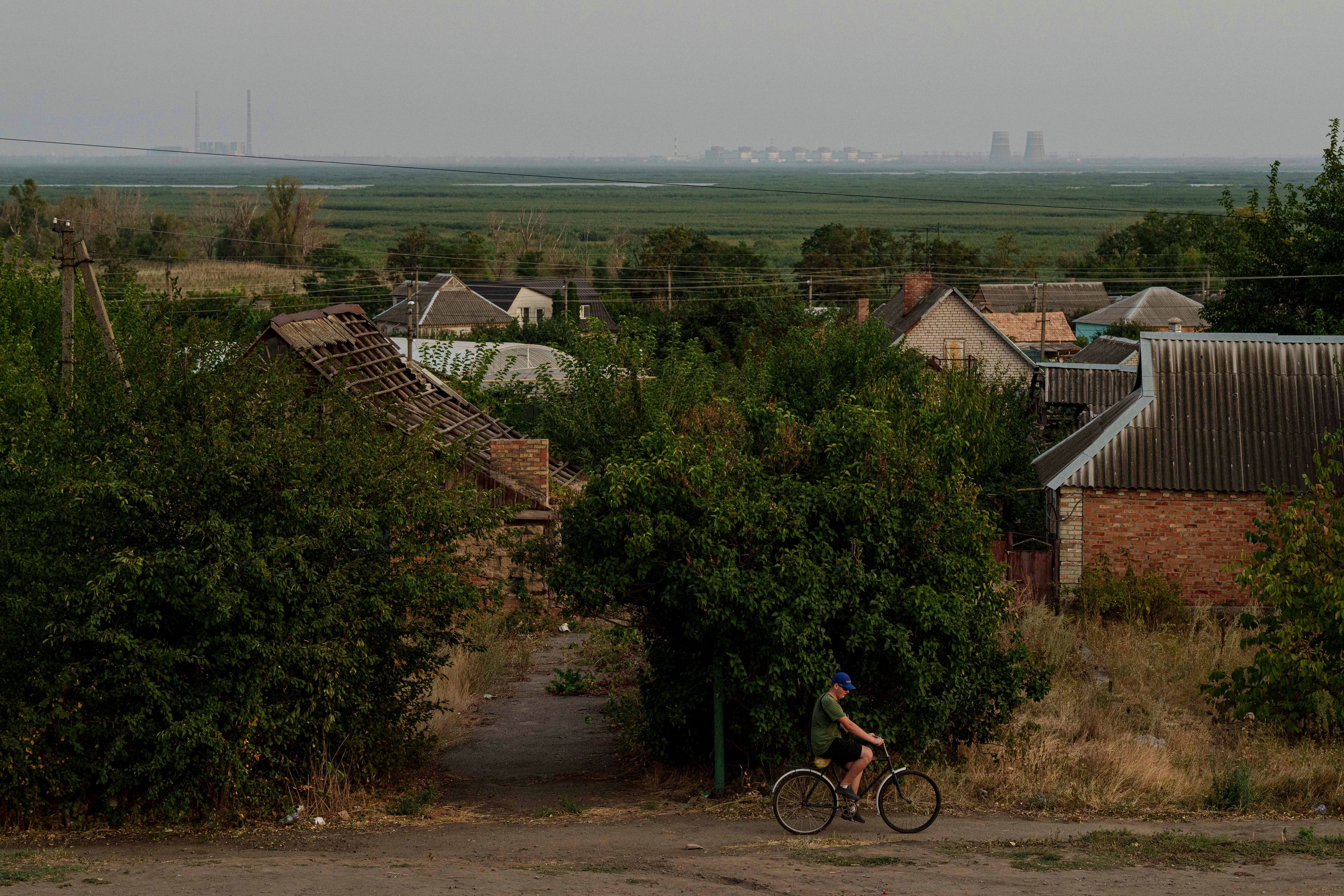 With the Zaporizhzhia nuclear power plant in the background, a bicyclist travels along a path in Nikopol, Ukraine, Sept. 2, 2024. Russian forces have controlled the plant since the first weeks of the war. (AP Photo/Evgeniy Maloletka)