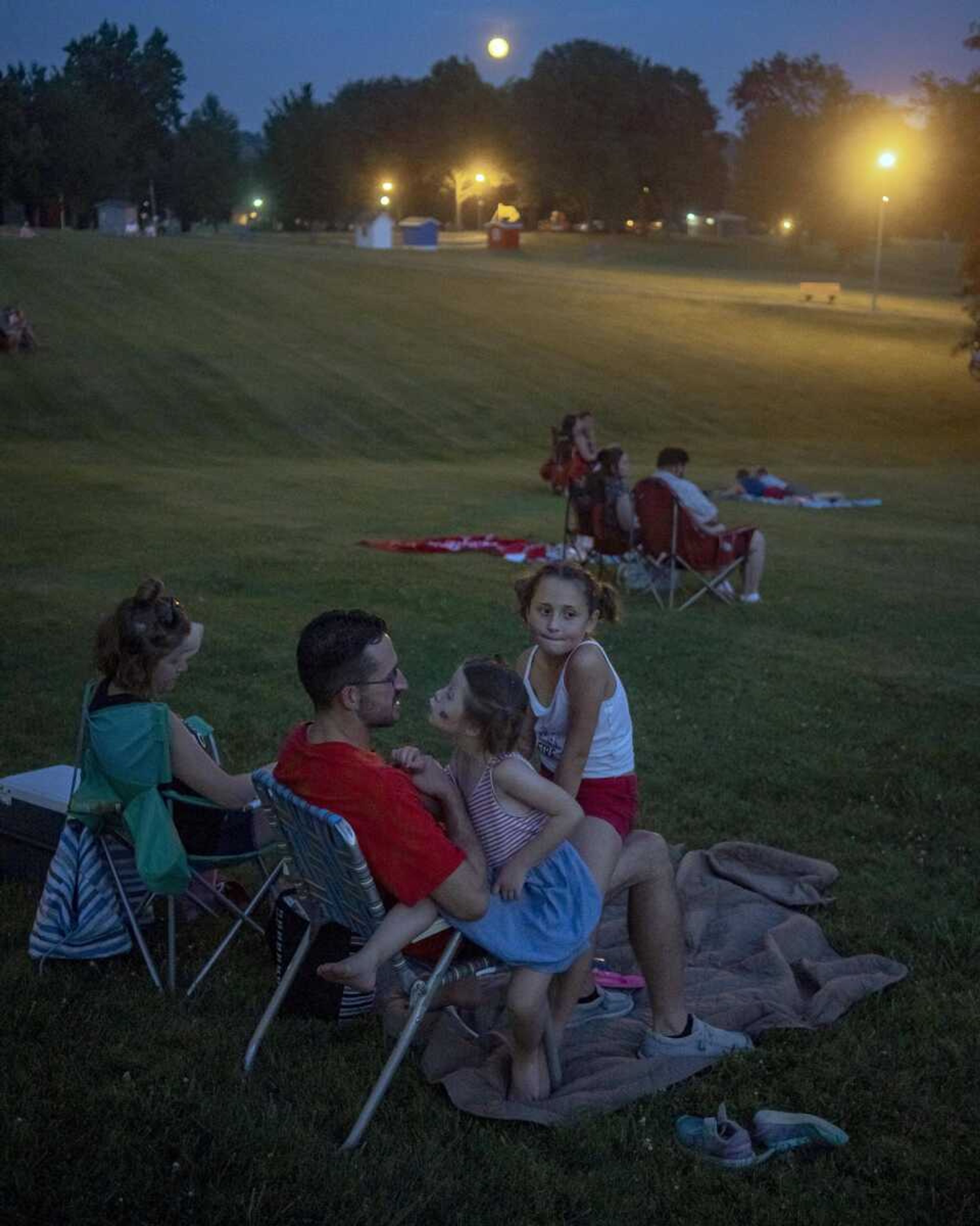 Harper Bruce, 8, right, and Averie Bruce, 6, sit on their father, Ryan Bruce's lap while waiting for a fireworks show at the Jackson Municipal Band Shell during an Independence Day celebration.