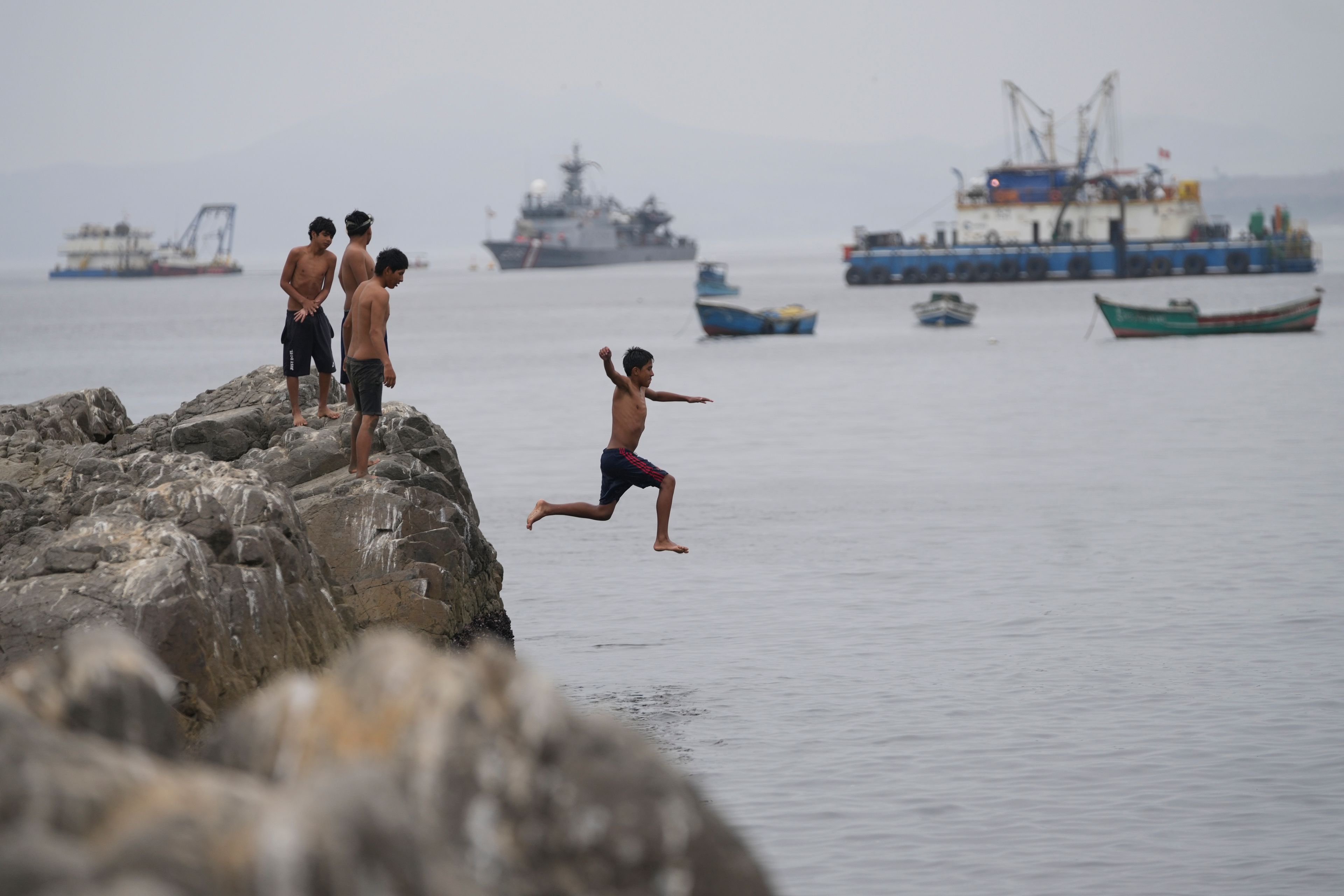 A youth jumps into the water near a Chinese-funded port in Chancay, Peru, Tuesday, Nov. 12, 2024. (AP Photo/Silvia Izquierdo)