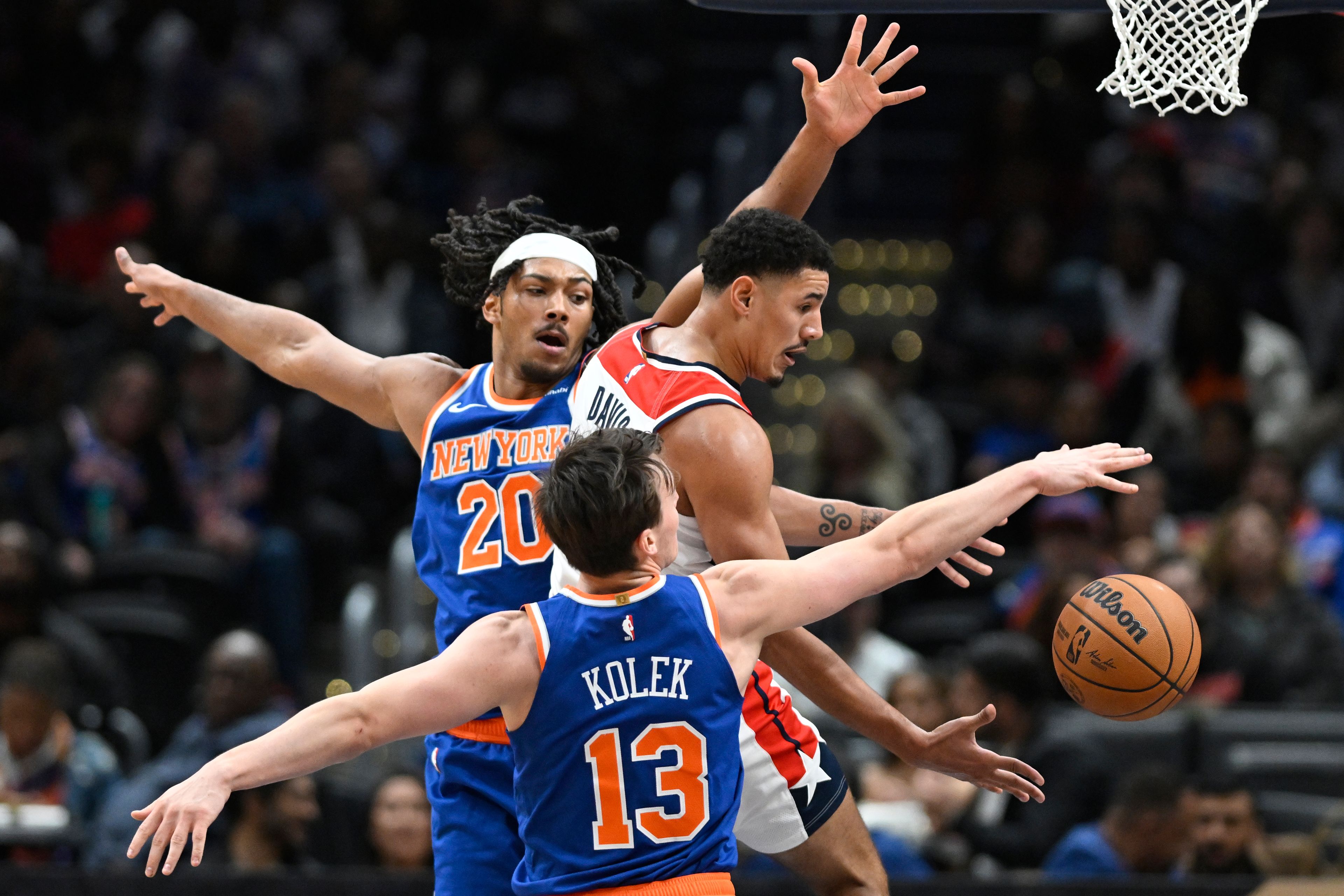 Washington Wizards guard Johnny Davis, top right, passes the ball off under the basket against New York Knicks center Jericho Sims (20) and Tyler Kolek (13) during the second half of an NBA preseason basketball game Friday, Oct. 18, 2024, in Washington. (AP Photo/John McDonnell)