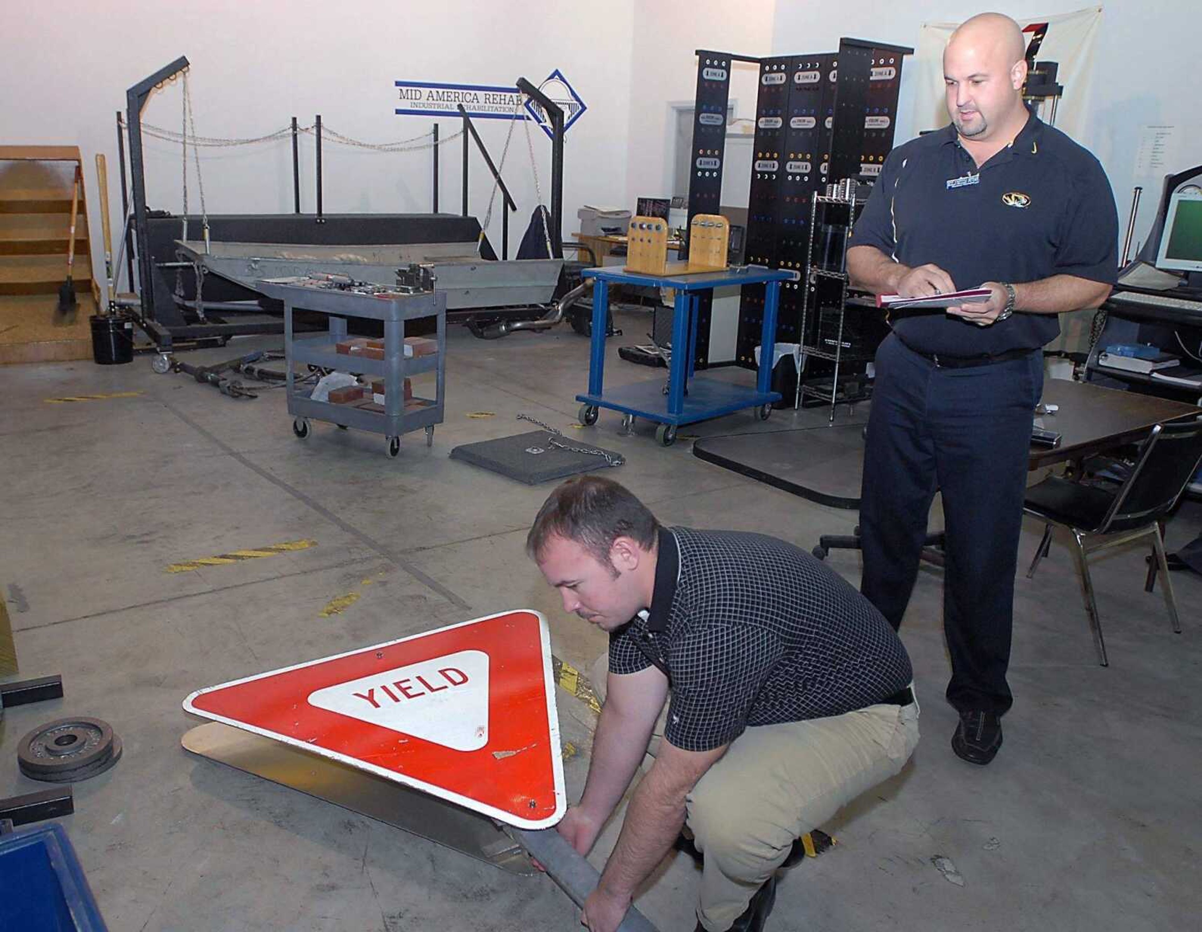 KIT DOYLE ~ kdoyle@semissourian.com<br>Jason Moore, left, and Bob Sherrill demonstrate a work-related skill test in the industrial rehabilitation area of Mid America Rehab Tuesday, January 6, 2008, in Cape Girardeau. Lifting a Yield sign is an example of what a Missouri Department of Transportation employee might see in a normal work day.